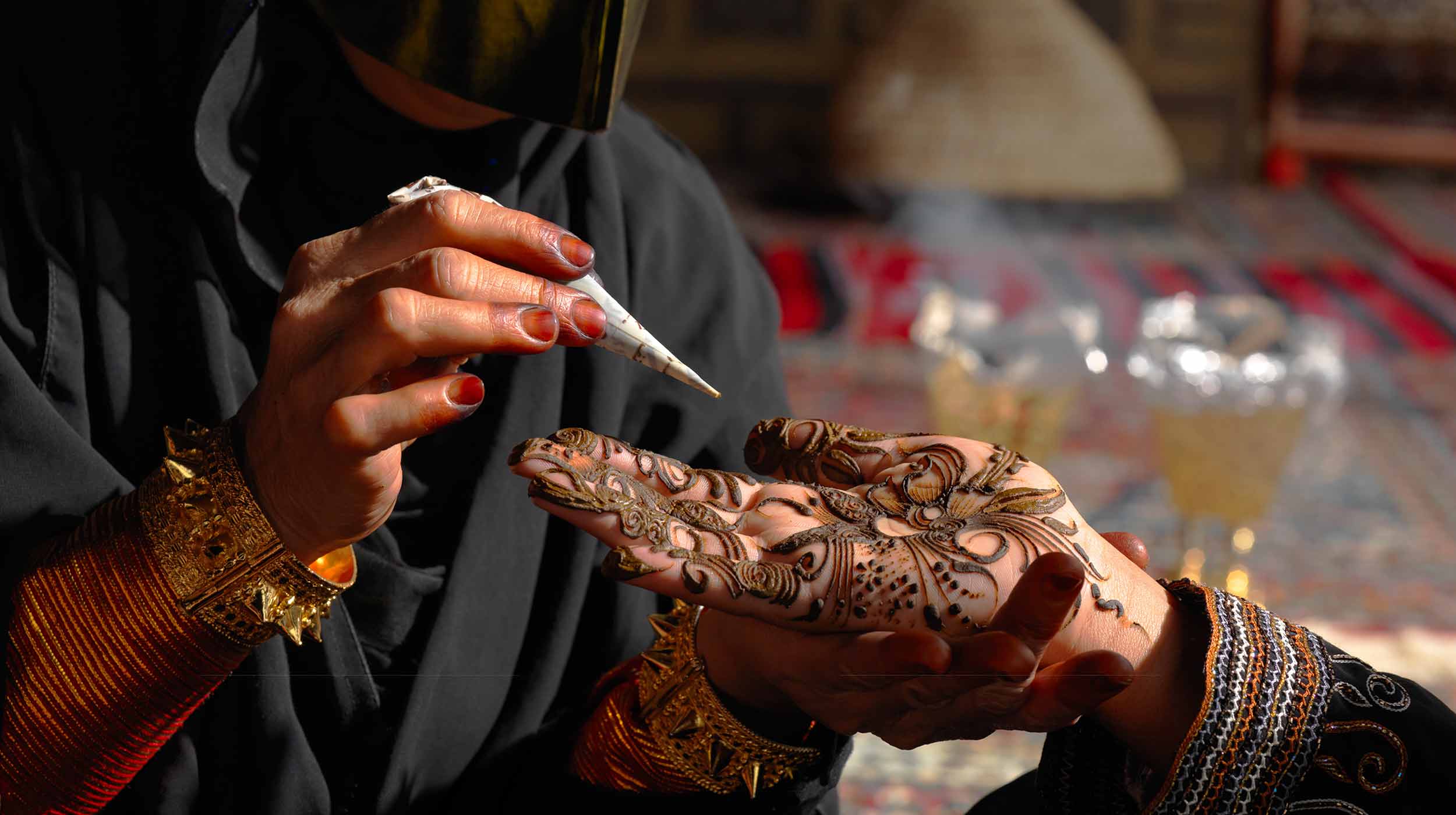 Ein Künstler verziert eine Damenhand mit einer traditionell kunstvollen Henna-Technik