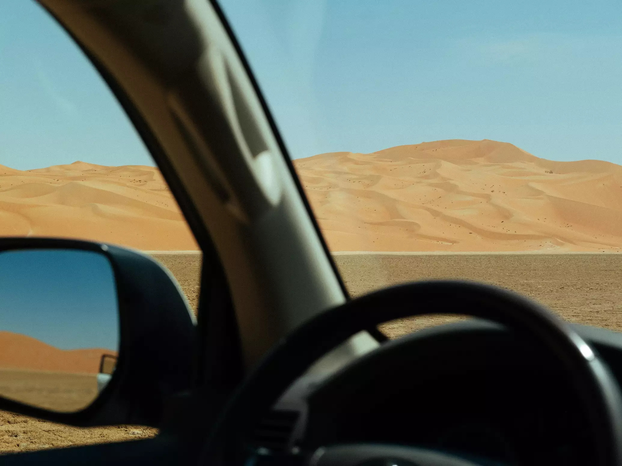RV side mirror on sandy beach with blue sky backdrop