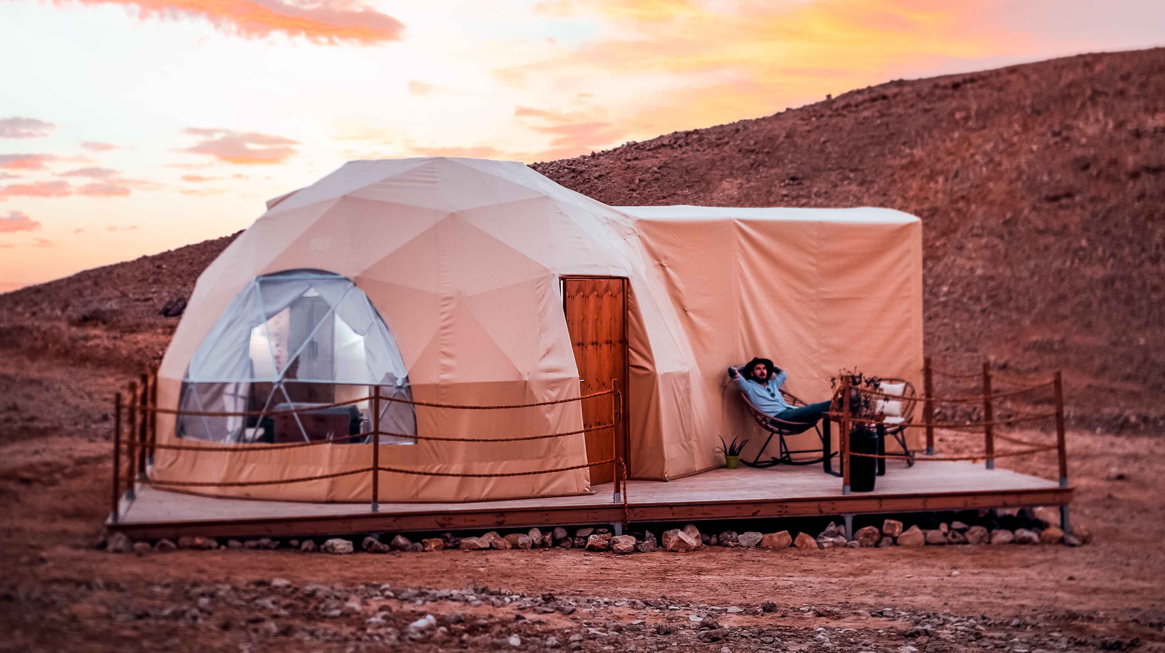 A cozy dome tent in the Abu Dhabi desert at sunset, with a man relaxing on the deck.