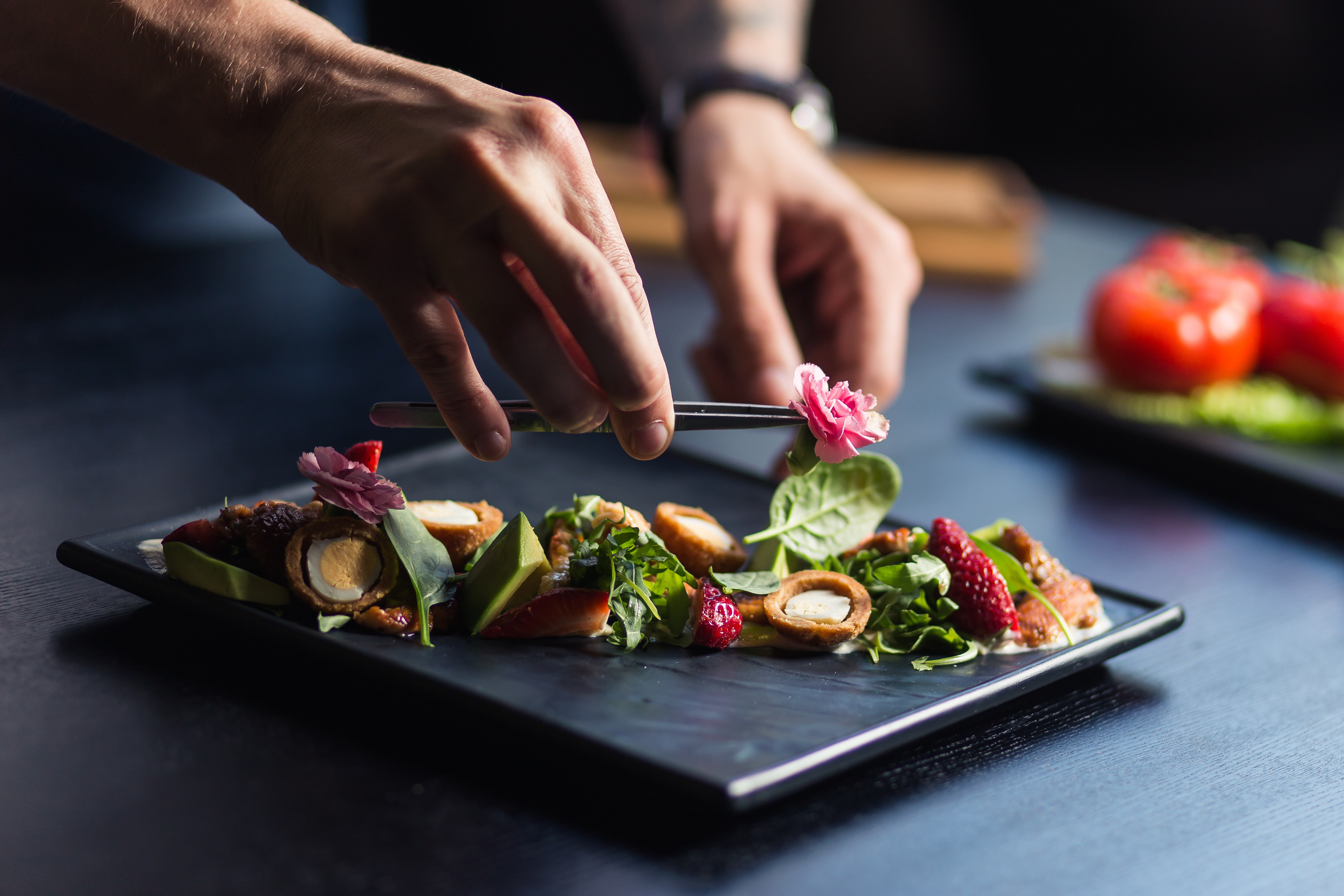 Chef placing edible flowers on a gourmet dish with avocado, greens, and strawberries in Abu Dhabi