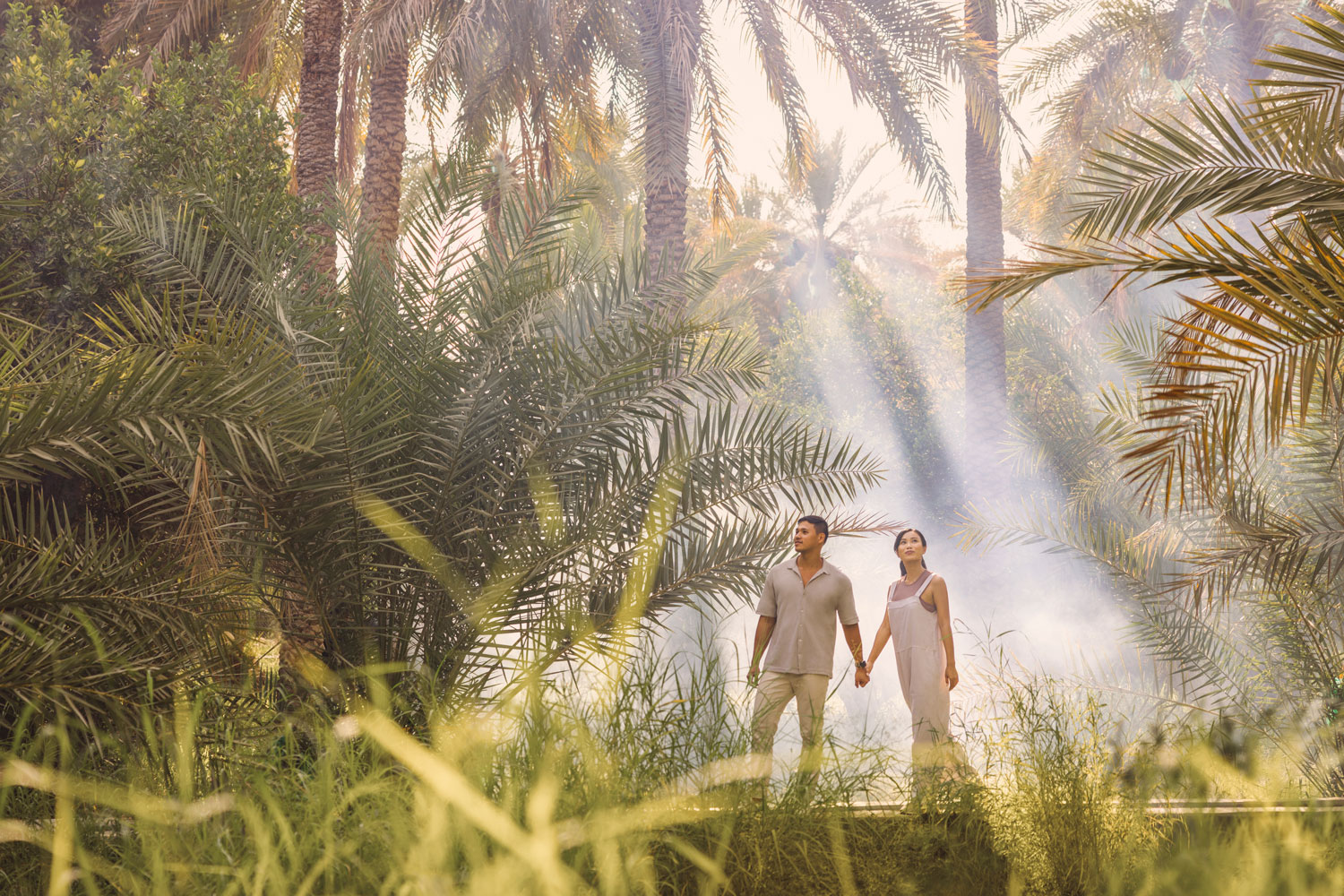 Couple enjoying a peaceful walk through Al Ain Oasis in Abu Dhabi, surrounded by lush palm groves and dappled sunlight filtering through the trees.