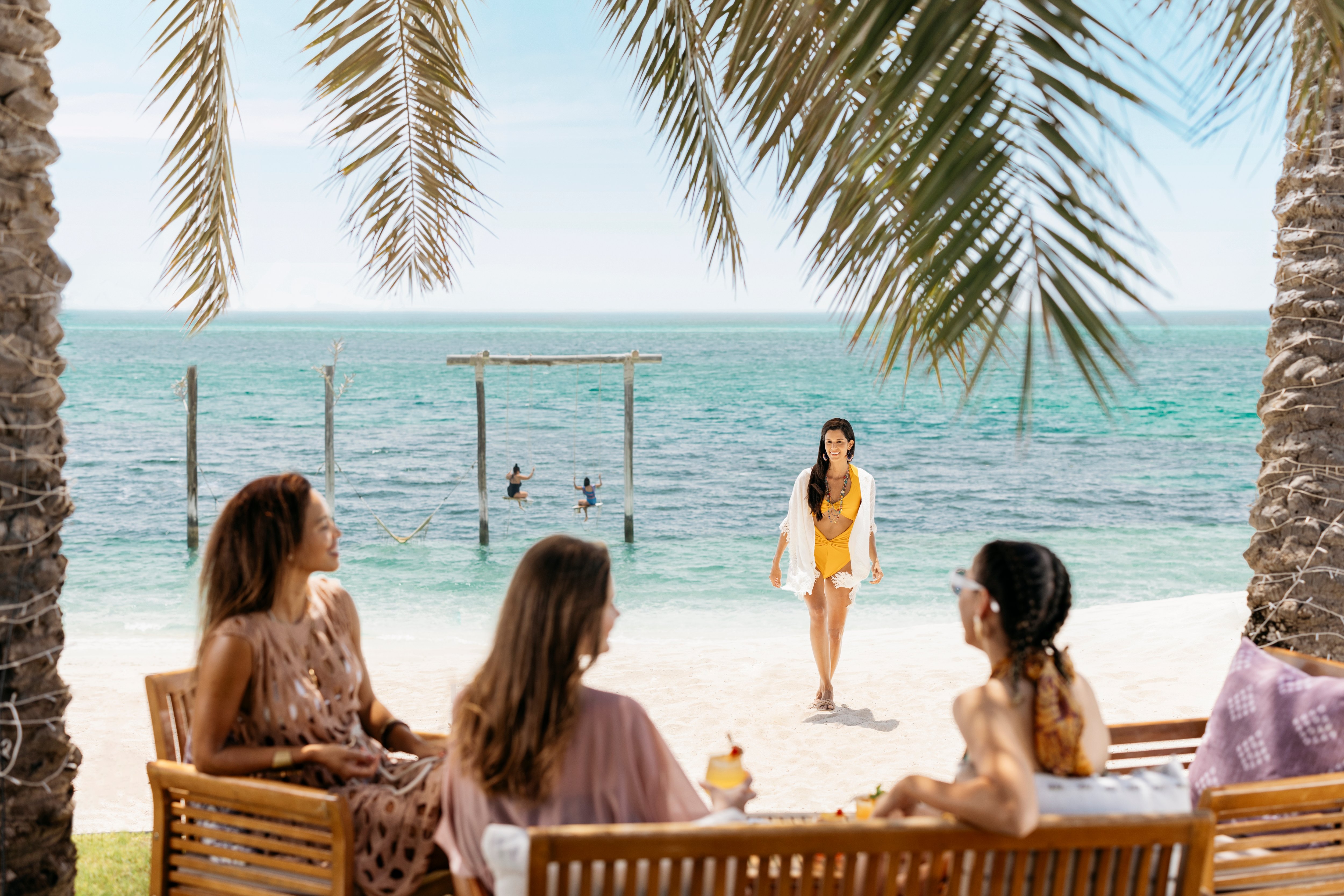 Female tourists in swimming costumes on Nurai Island beach, drinking cocktails