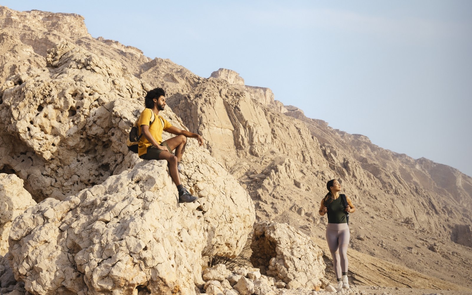 زوجان أجنبيان يستمتعان بالمشي وسط الجبال الصخرية في إمارة أبوظبي