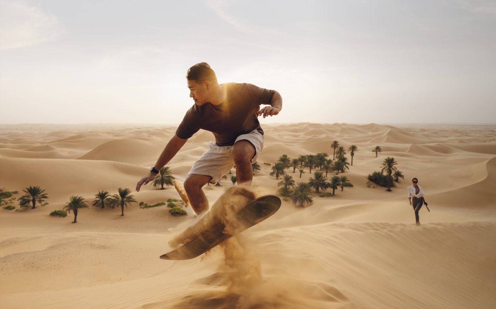 رجل صيني يقوم بالتزلج باللوح فوق الرمال في صحراء أبوظبي