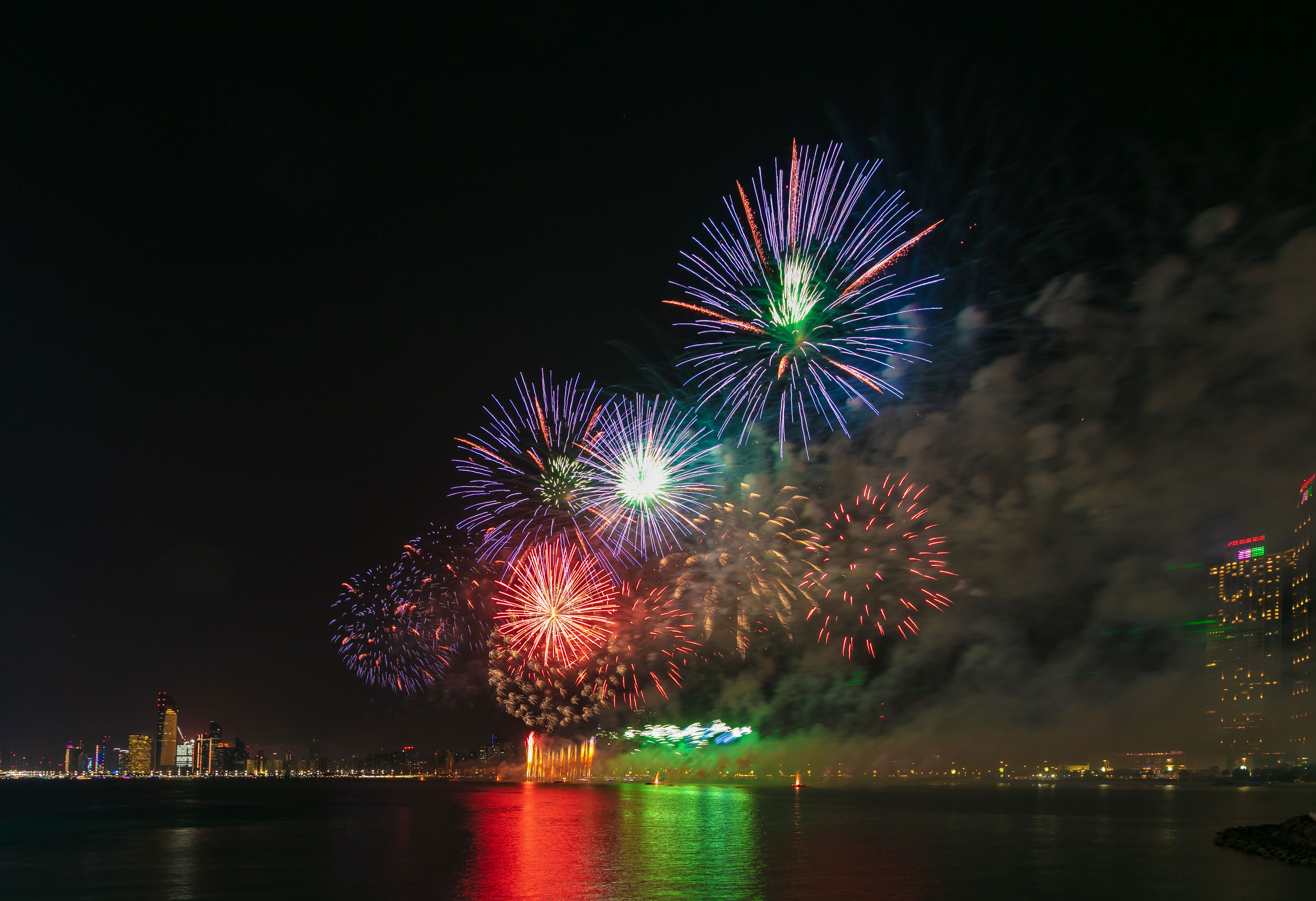Spectacular fireworks in red, green, and blue light up Abu Dhabi's night sky over the waterfront cityscape.