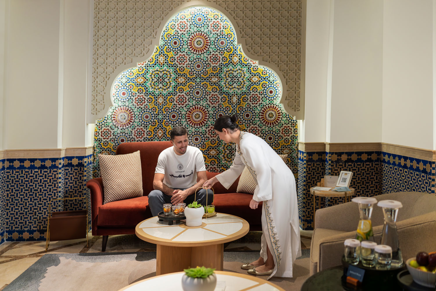 Guest being served traditional refreshments in a Moroccan-inspired lounge with vibrant mosaic tiles.