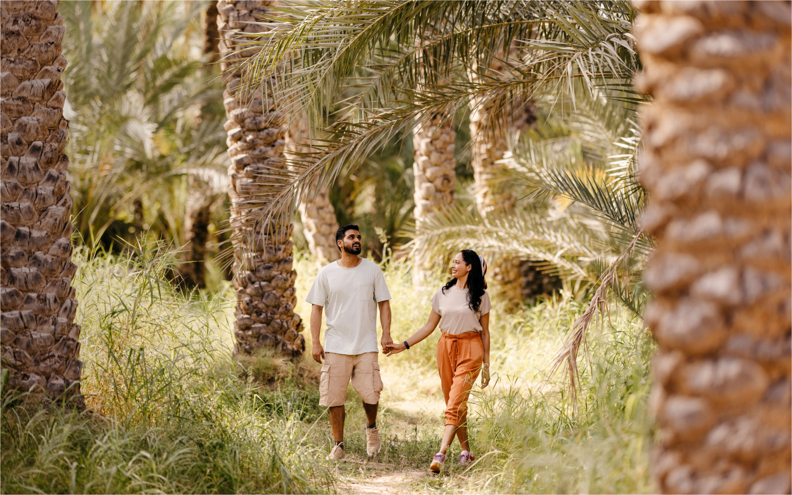Couple holding hands while walking through a lush palm tree grove.
