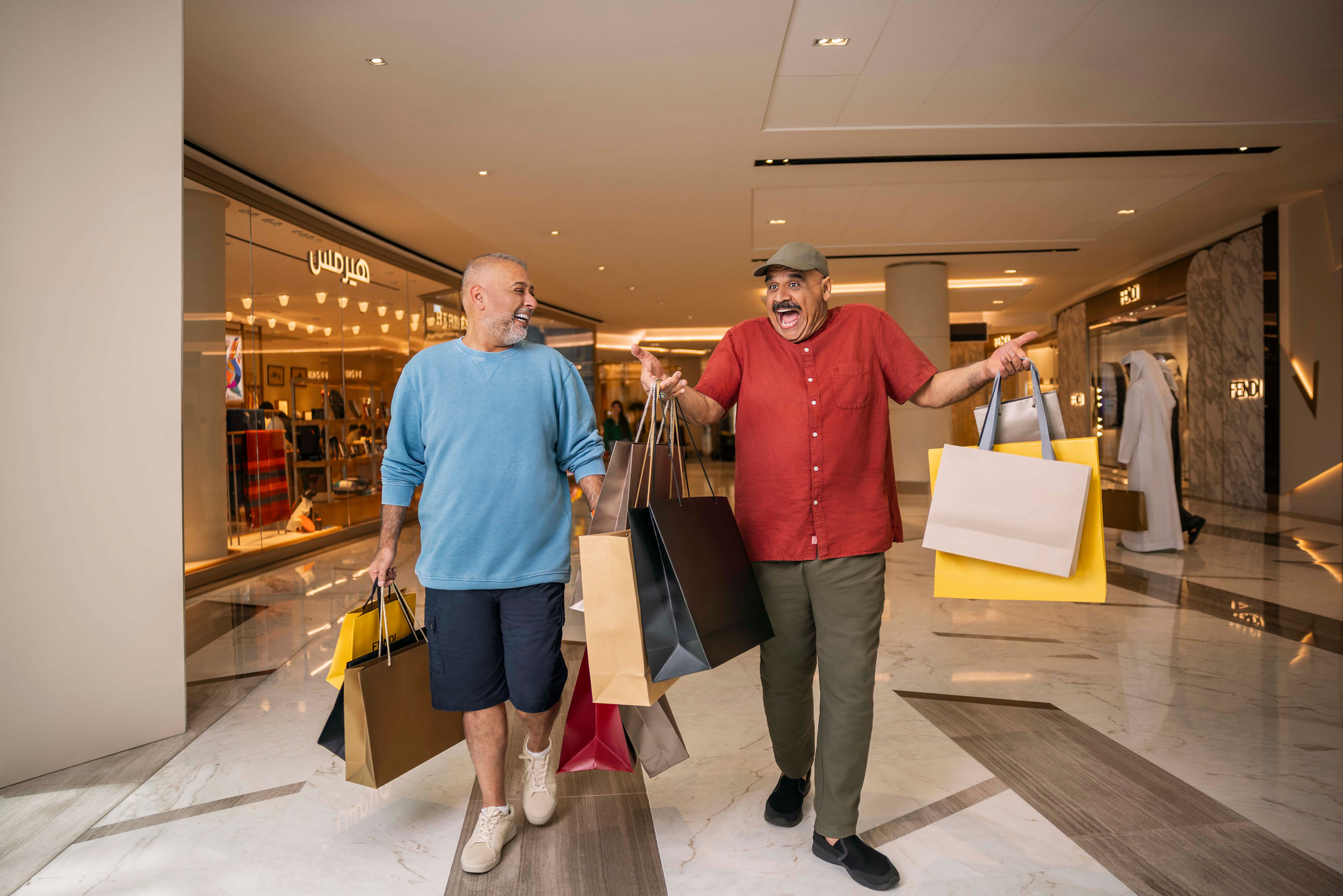 Two cheerful men walking through a luxury Abu Dhabi mall with shopping bags in hand.