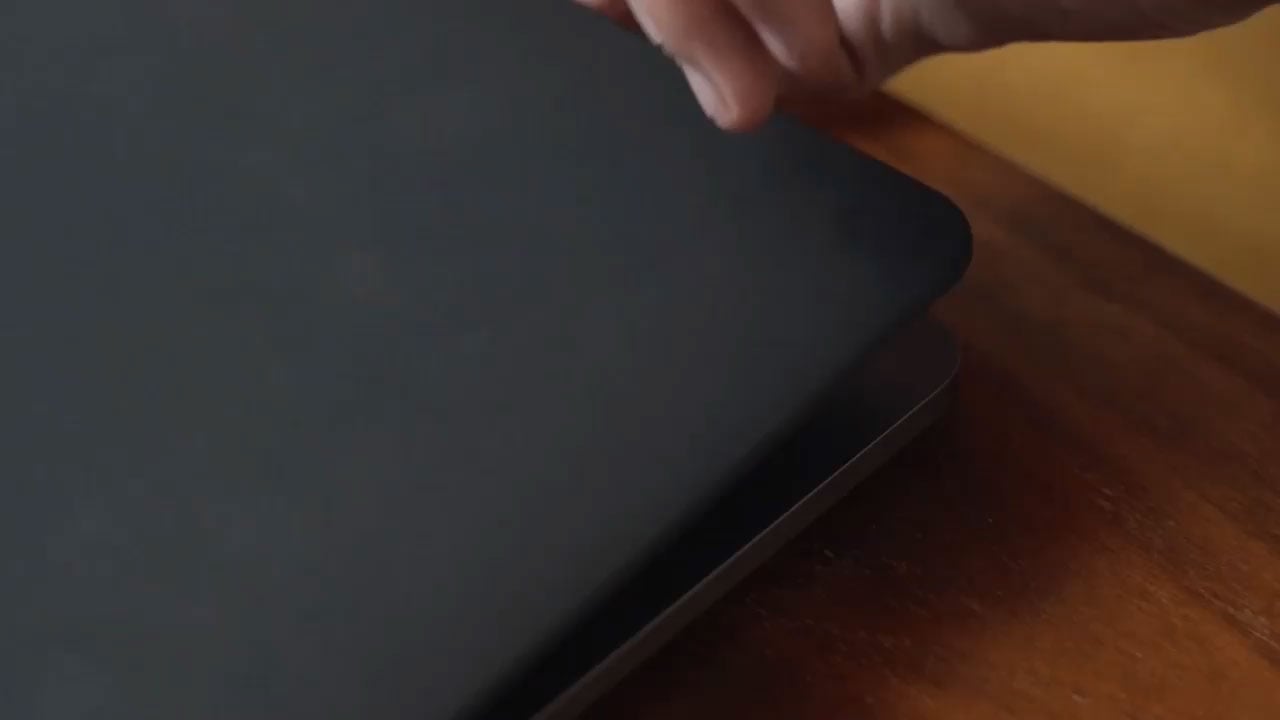 Hand closing a black laptop on a wooden desk in warm lighting