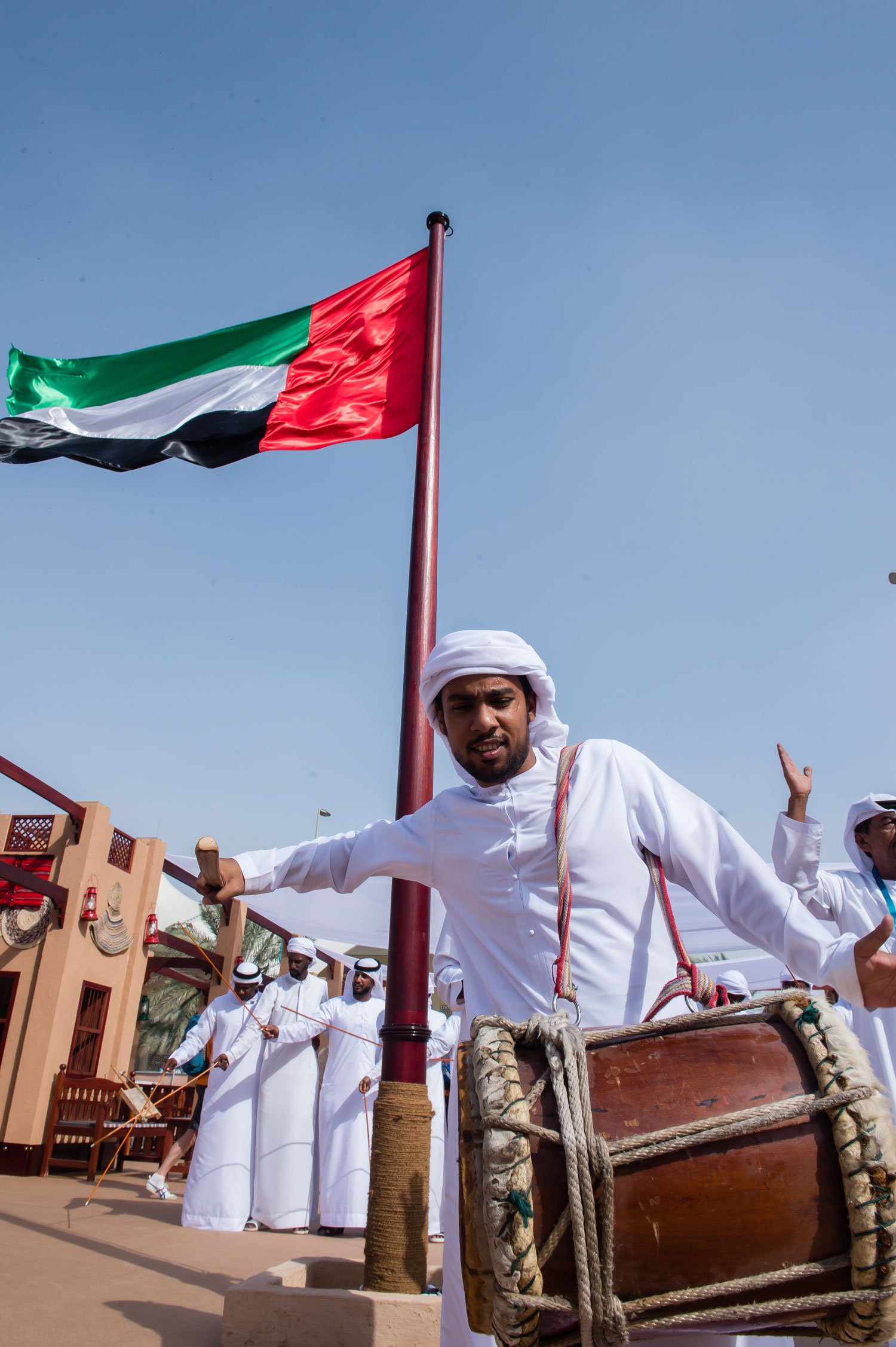 Emirati man playing traditional drum under UAE flag during cultural celebration in Abu Dhabi