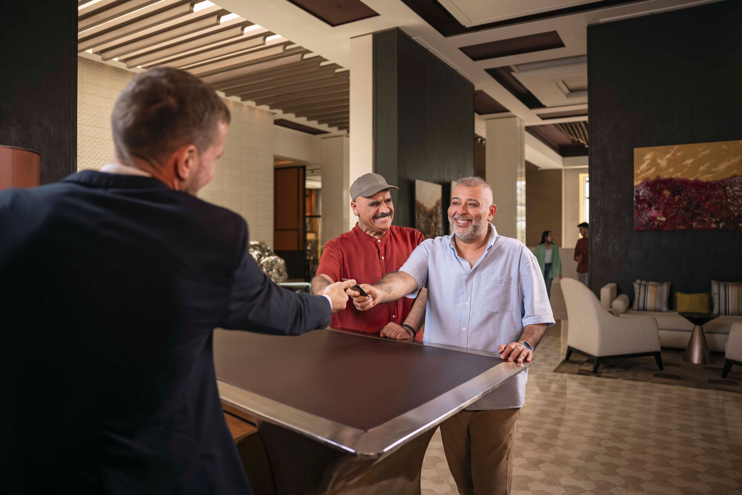 Two men happily checking into a luxury Abu Dhabi hotel, greeted warmly at the reception desk by staff.