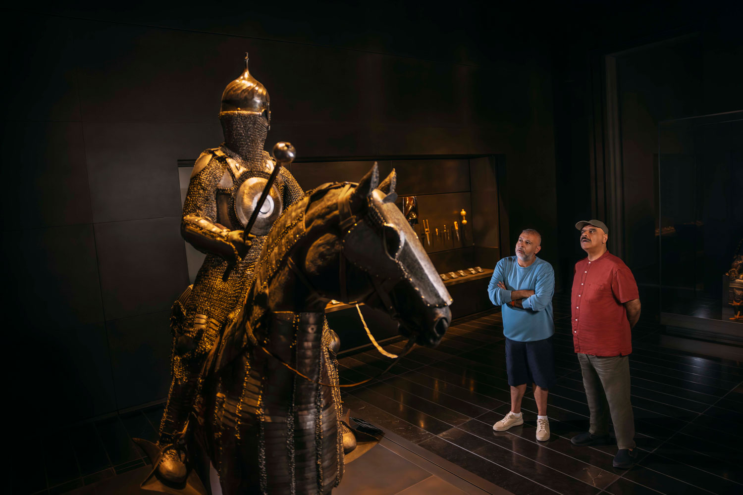 Two men admiring an ancient armored warrior and horse exhibit at a cultural museum in Abu Dhabi.