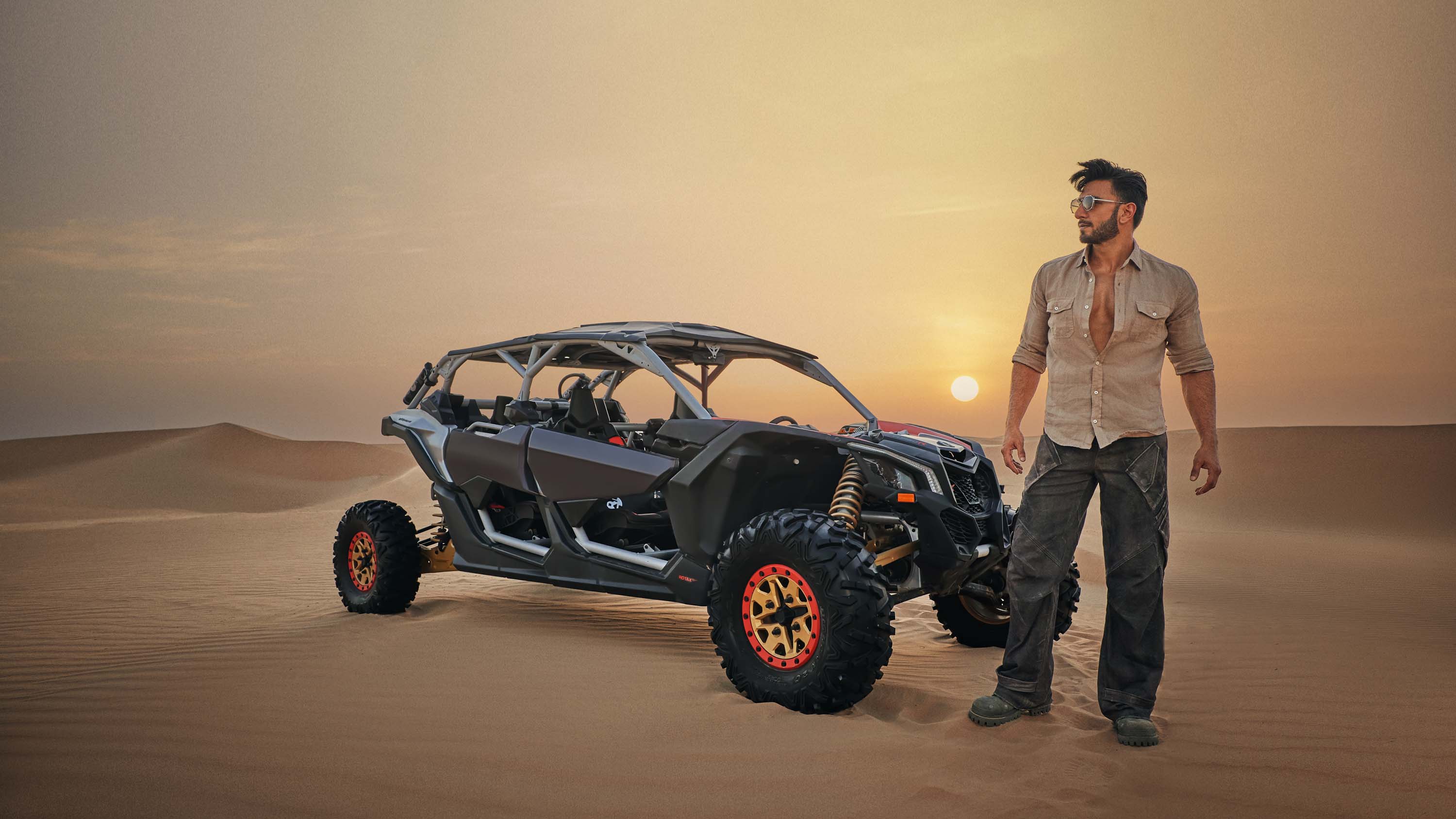 Man standing next to a black dune buggy in the desert during sunset, with sand dunes in the background