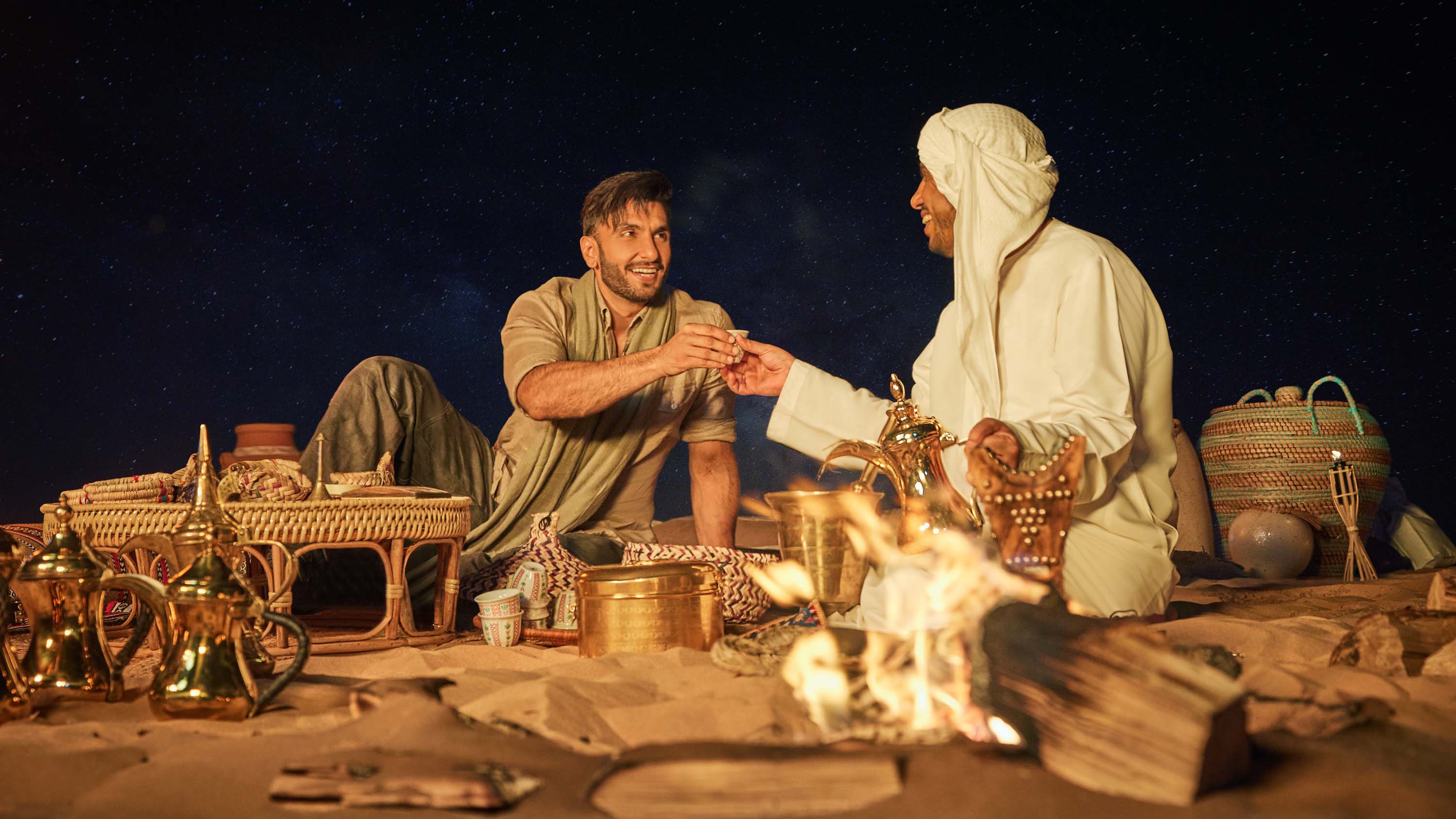 Two men enjoying traditional Arabic coffee by a campfire under a starry desert sky at night