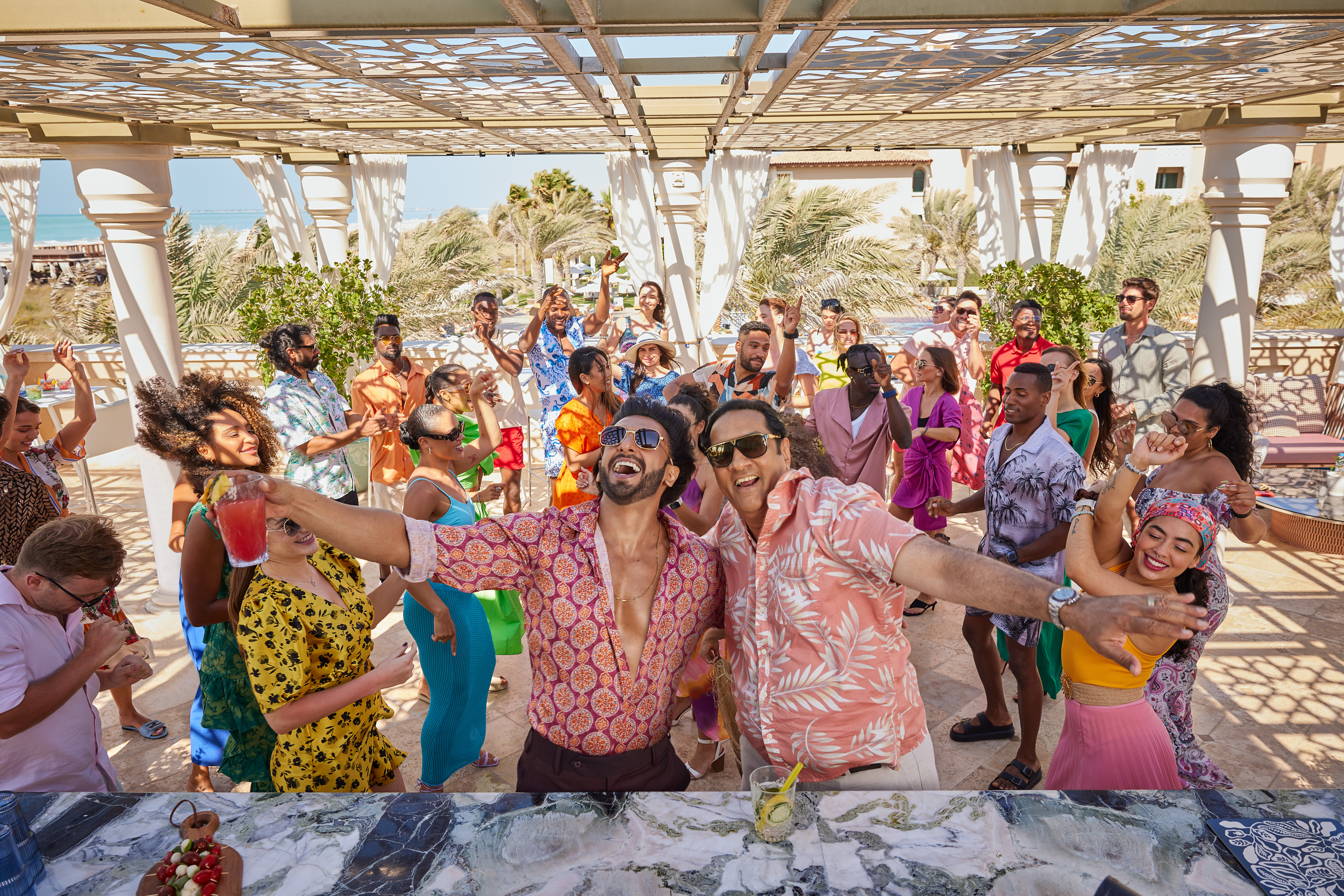Group of friends enjoying a vibrant beachside party with dancing, cocktails, and summer outfits