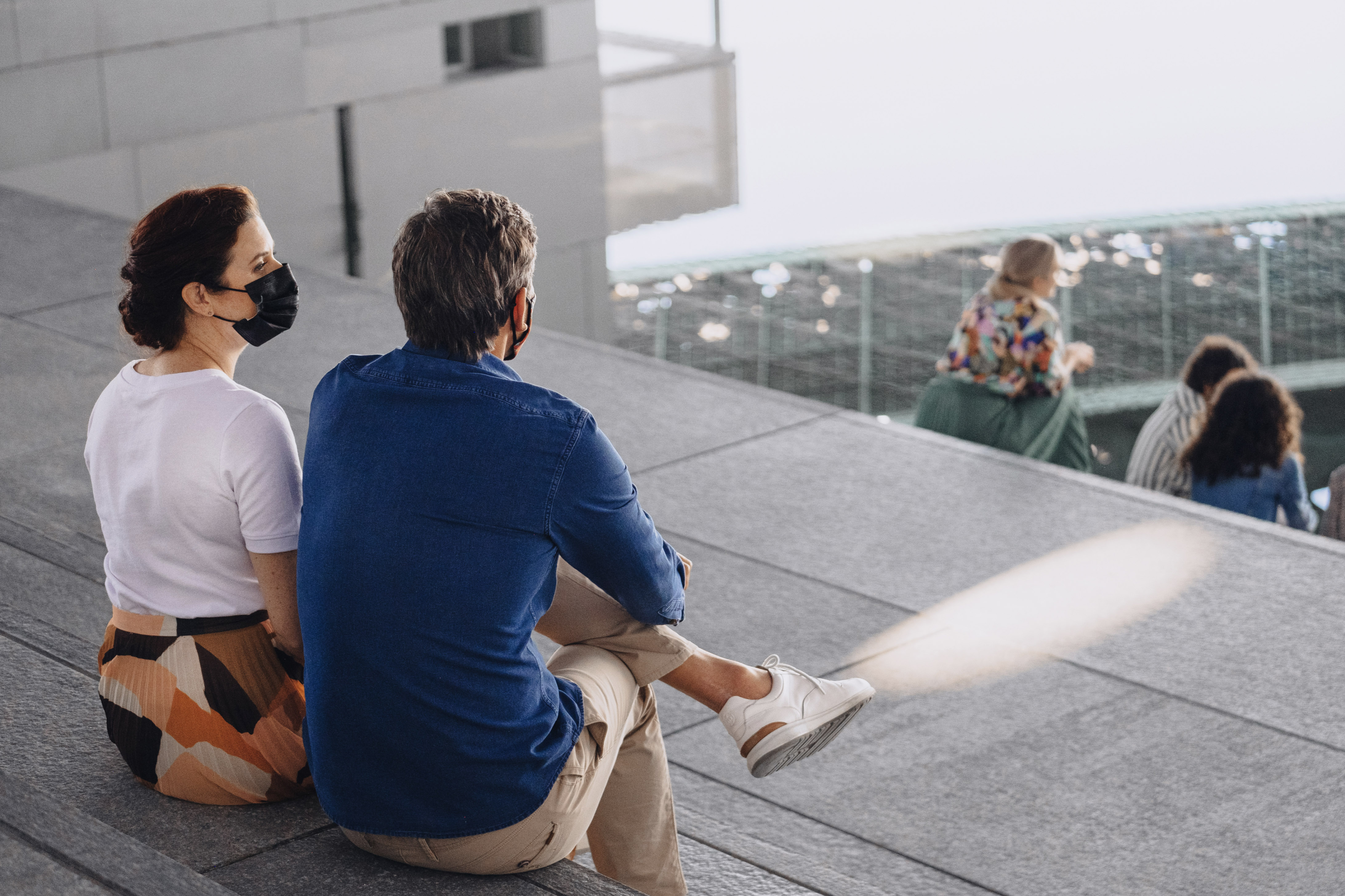 Couple wearing masks and sitting on the steps in front of the Louvre Abu Dhabi