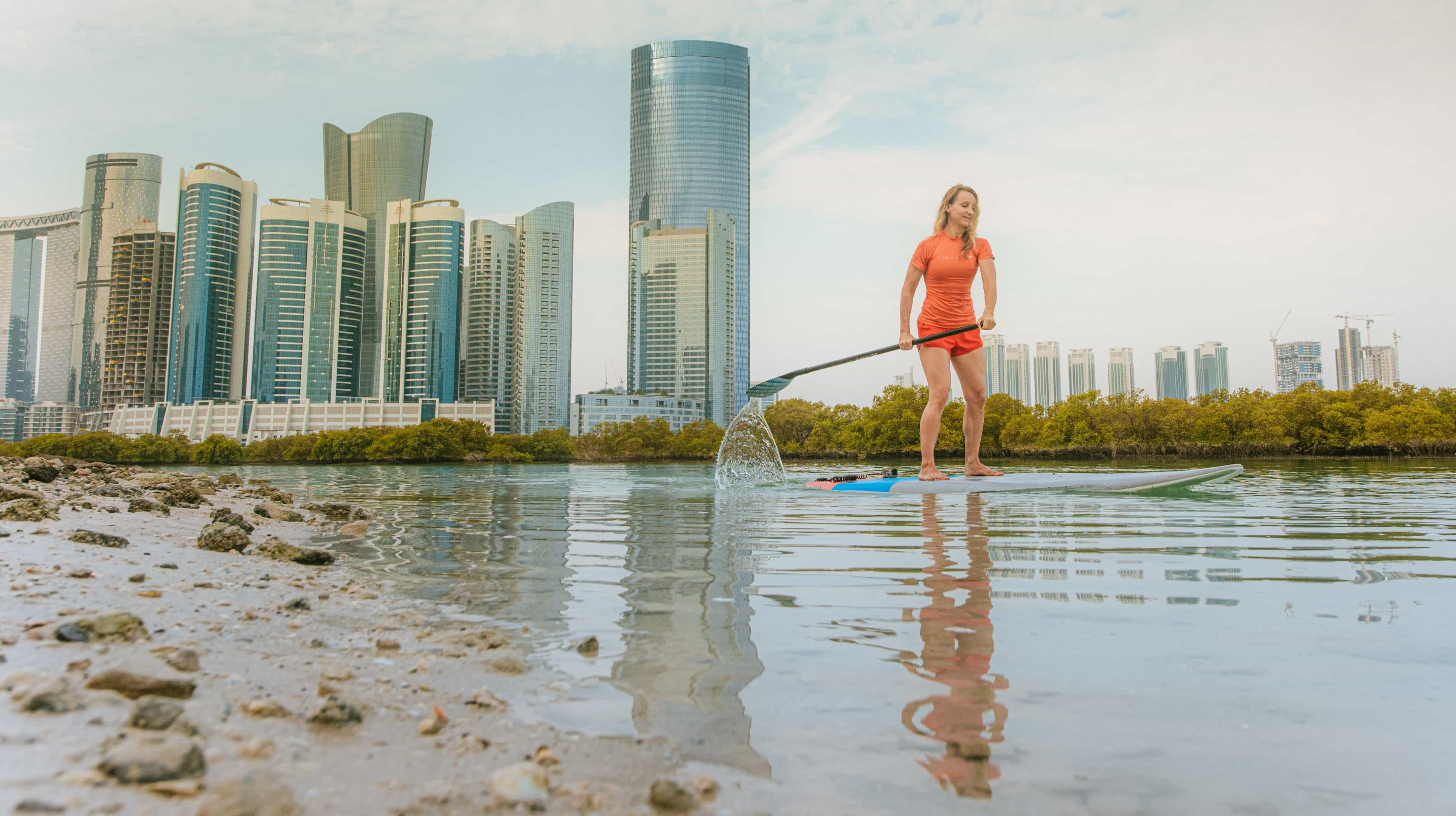Eine blonde junge Frau paddelt in Abu Dhabi vor dem Hintergrund von Wolkenkratzern