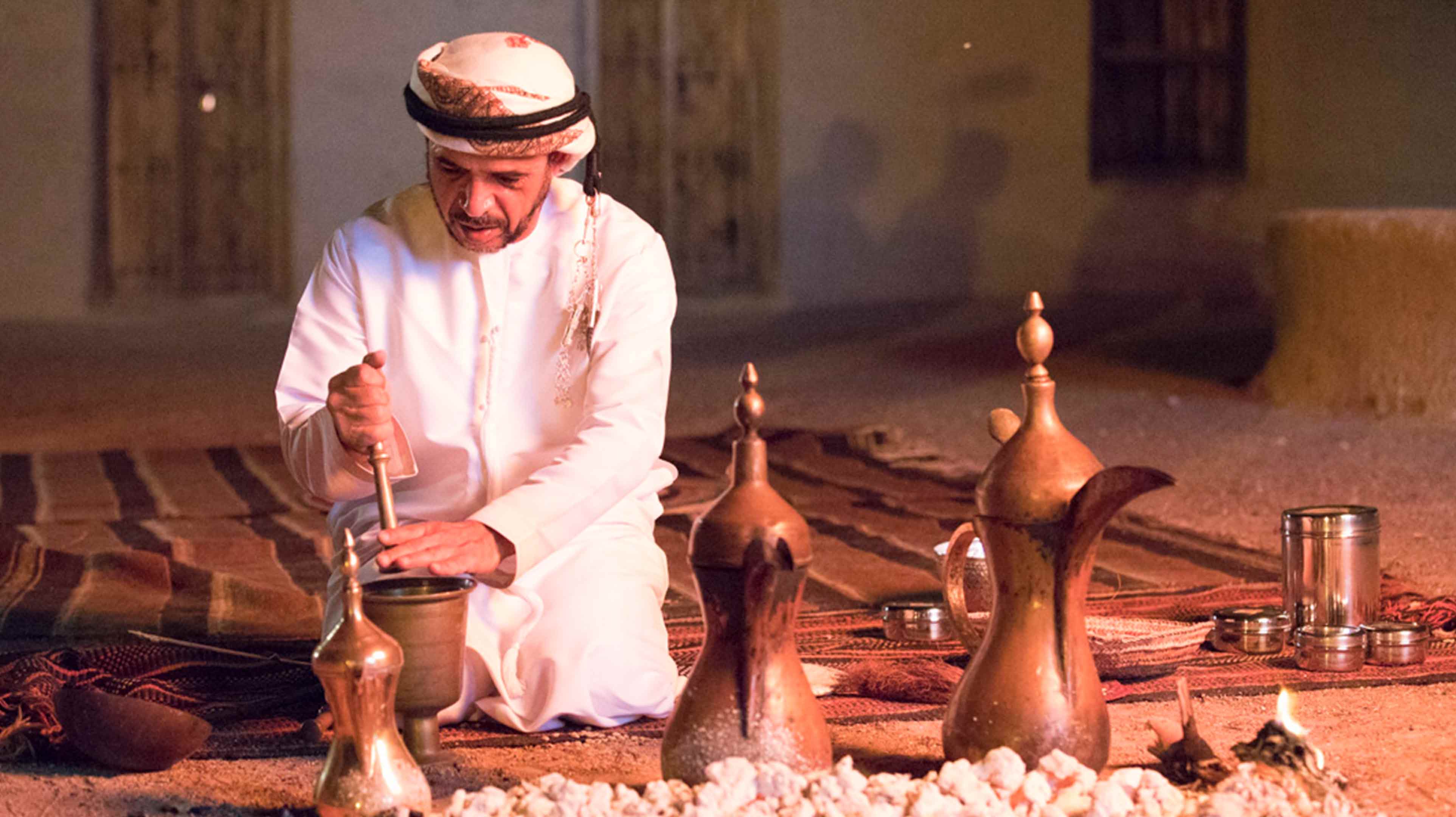 Emirati man crushing beans for a traditional coffee