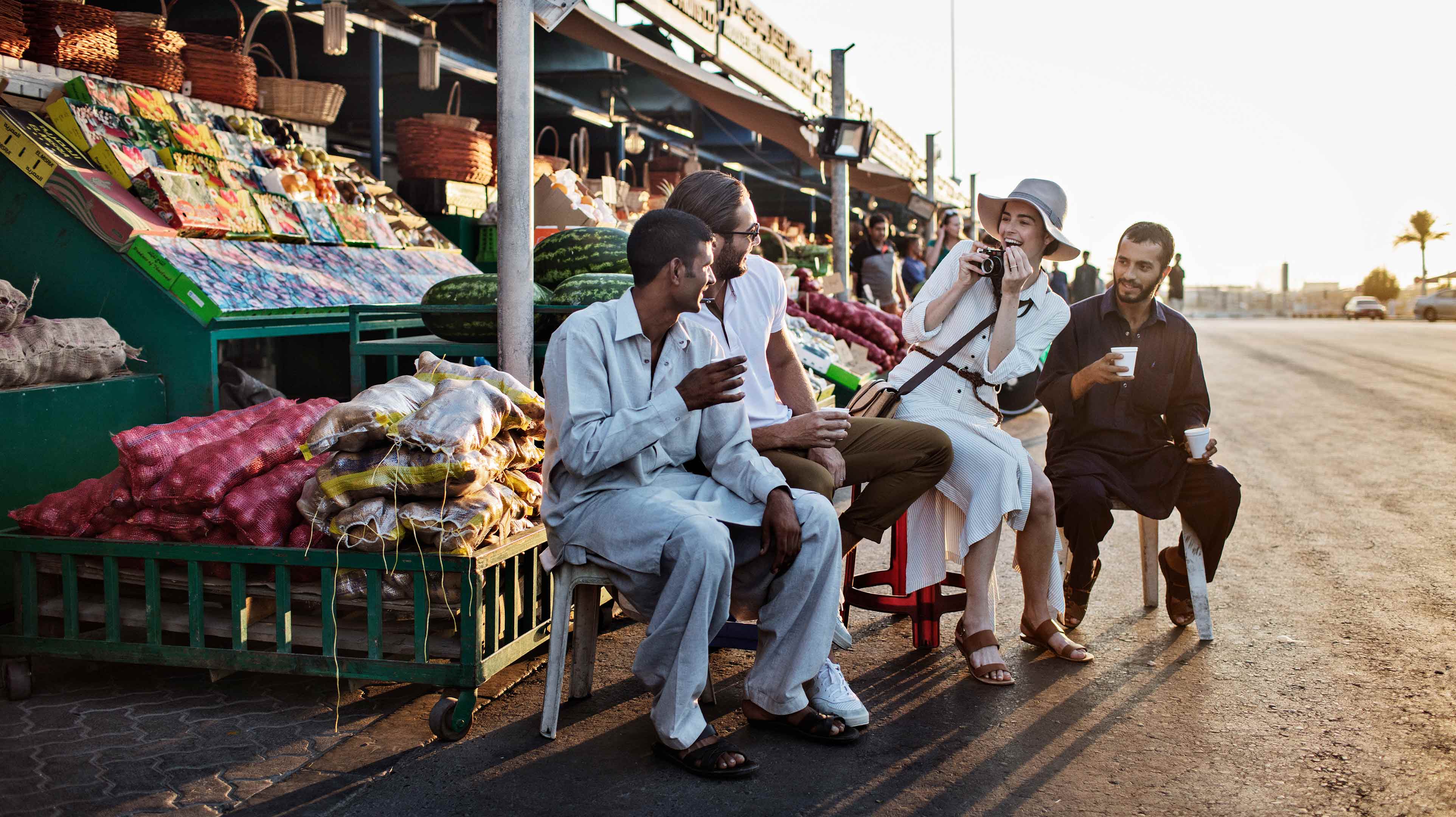 Tourists taking photos with a seller at a fruit and vegetable stall in the Mina Market