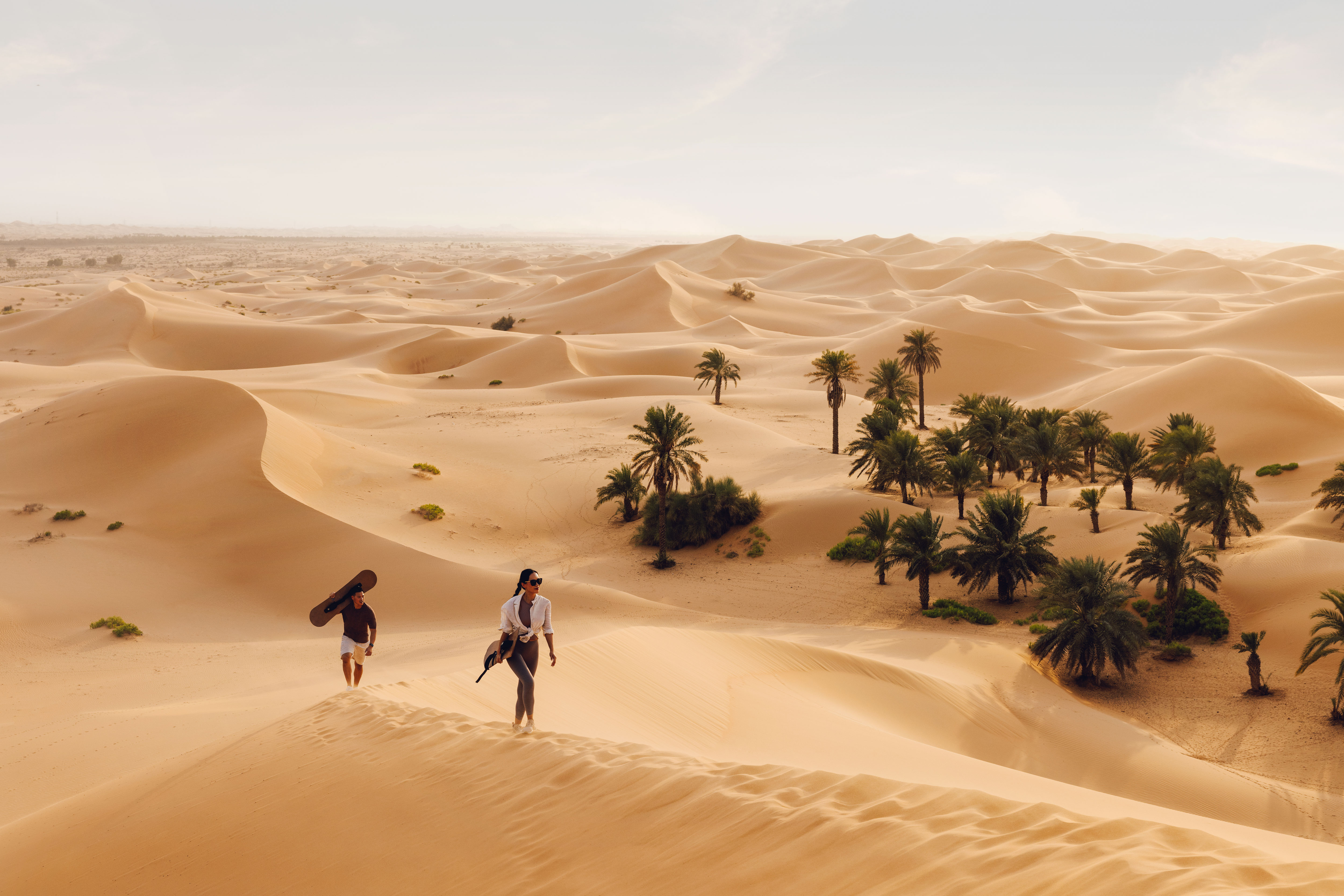 Woman and man walking in the Abu Dhabi desert dunes with sandboards