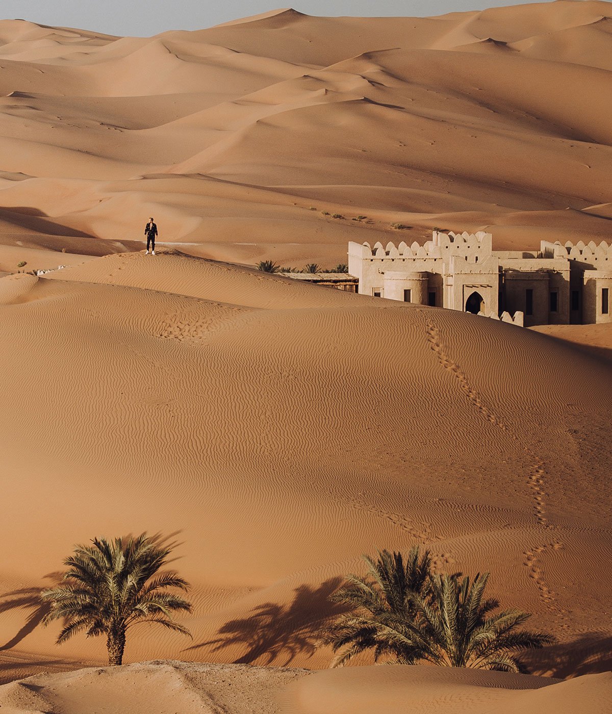 Abu Dhabi sand dunes and building with a man exploring and leaving footprints