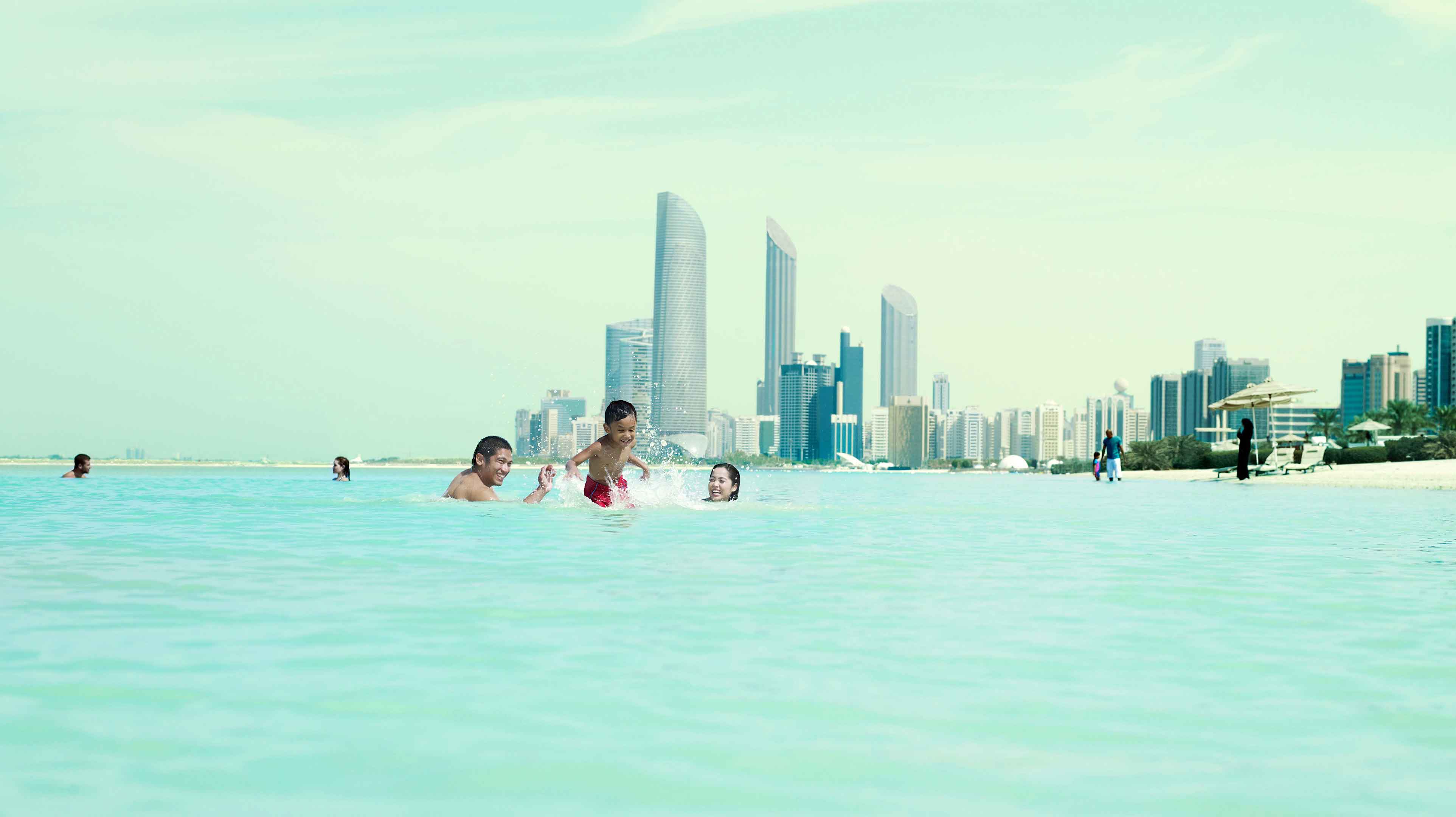 عائلة آسيوية تستمتع بالسباحة في البحر في كورنيش أبوظبي