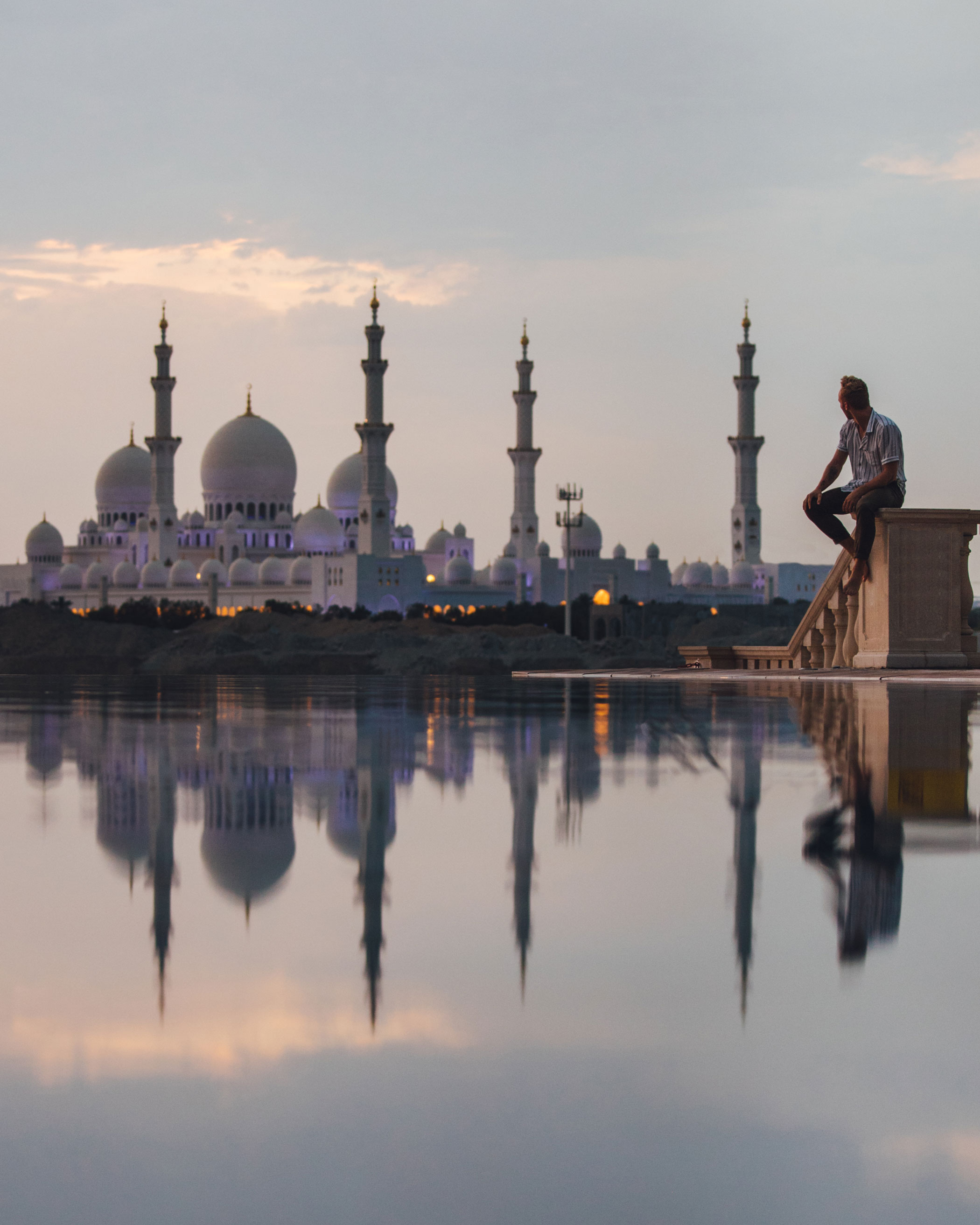 Face à la Grande Mosquée Cheikh Zayed, un visiteur contemple les reflets paisibles du bassin, saisi par la grandeur et la beauté sacrée du lieu.