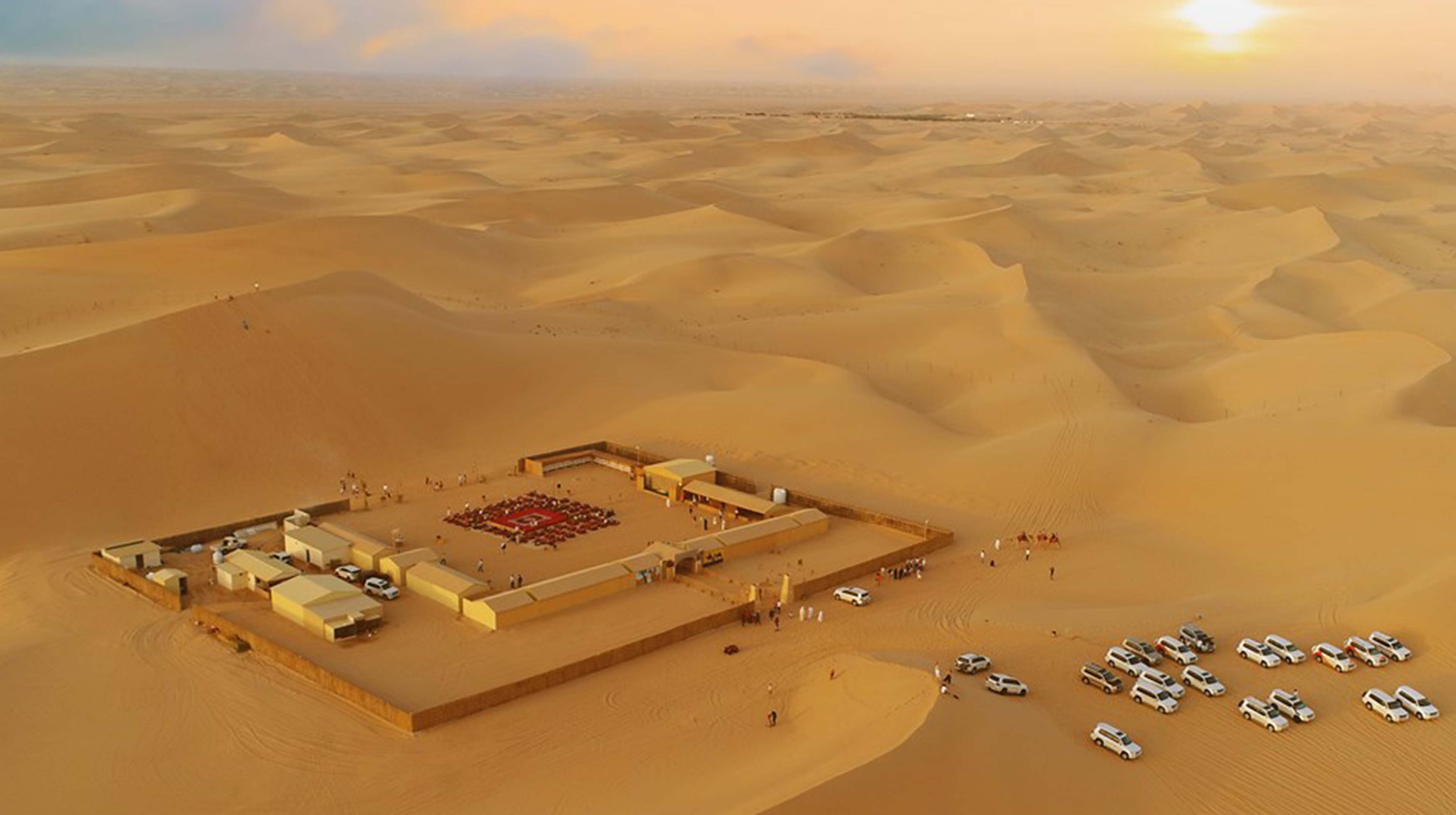 Vista dall'alto del Desert Rose Bedouin Camp tra le sabbie del deserto con jeep, uomini e tappeti tradizionali