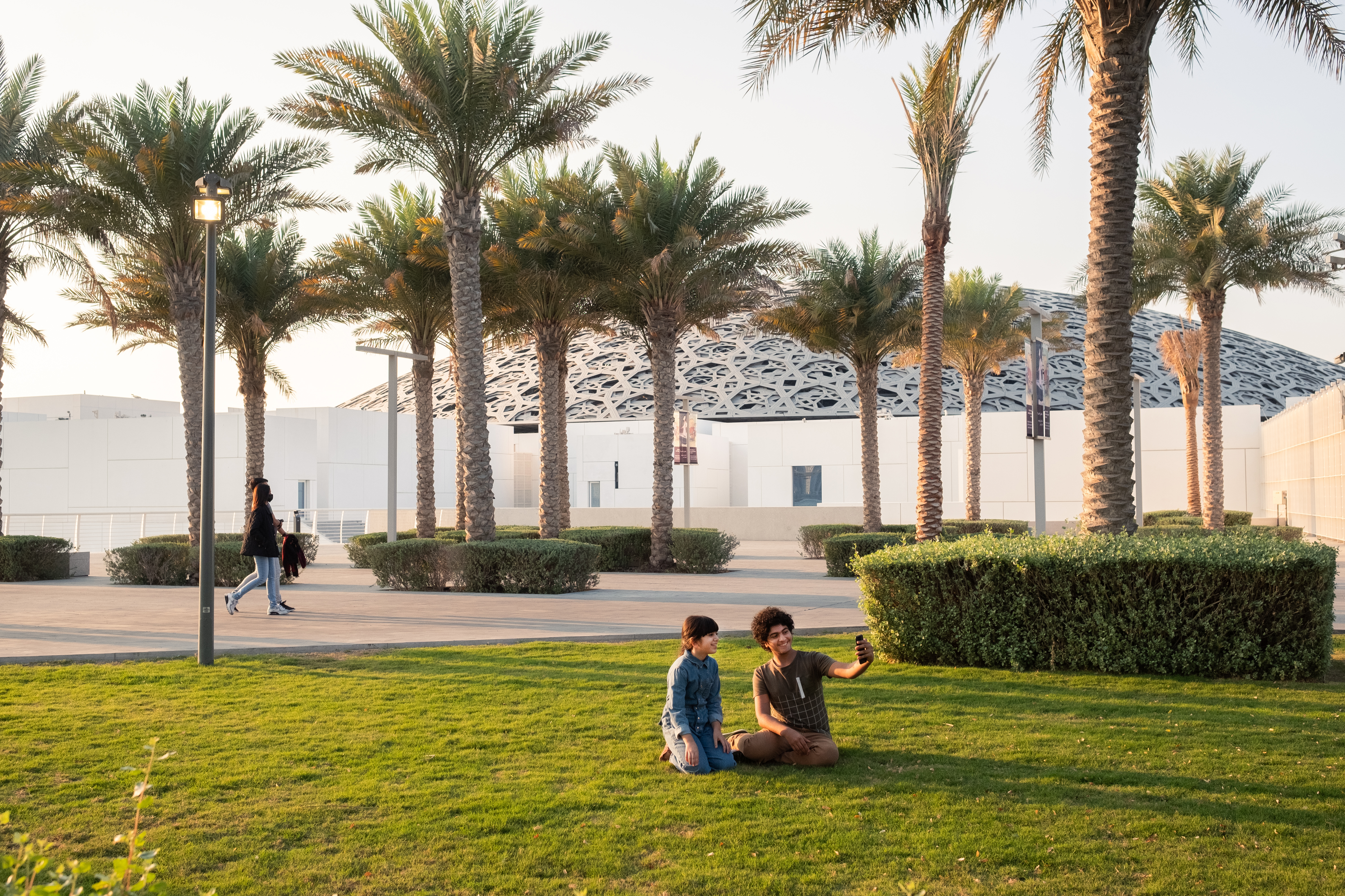 Due ragazzi sorridenti si scattano un selfie sul prato davanti al Louvre di Abu Dhabi