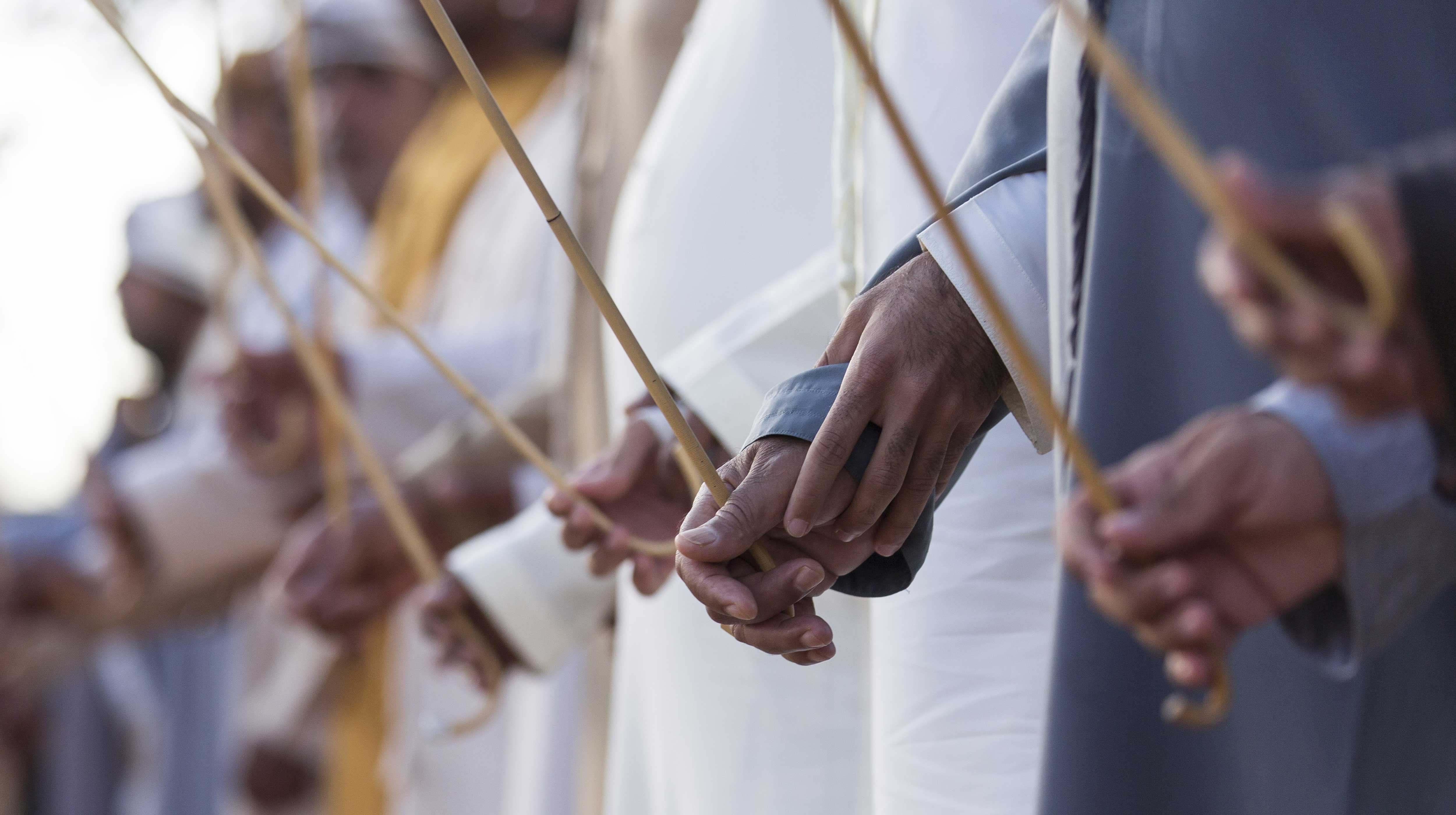 Primo piano delle mani di uomini emiratini che eseguono la danza tradizionale Al Ayala con bastoni di bambù in fila durante una celebrazione culturale