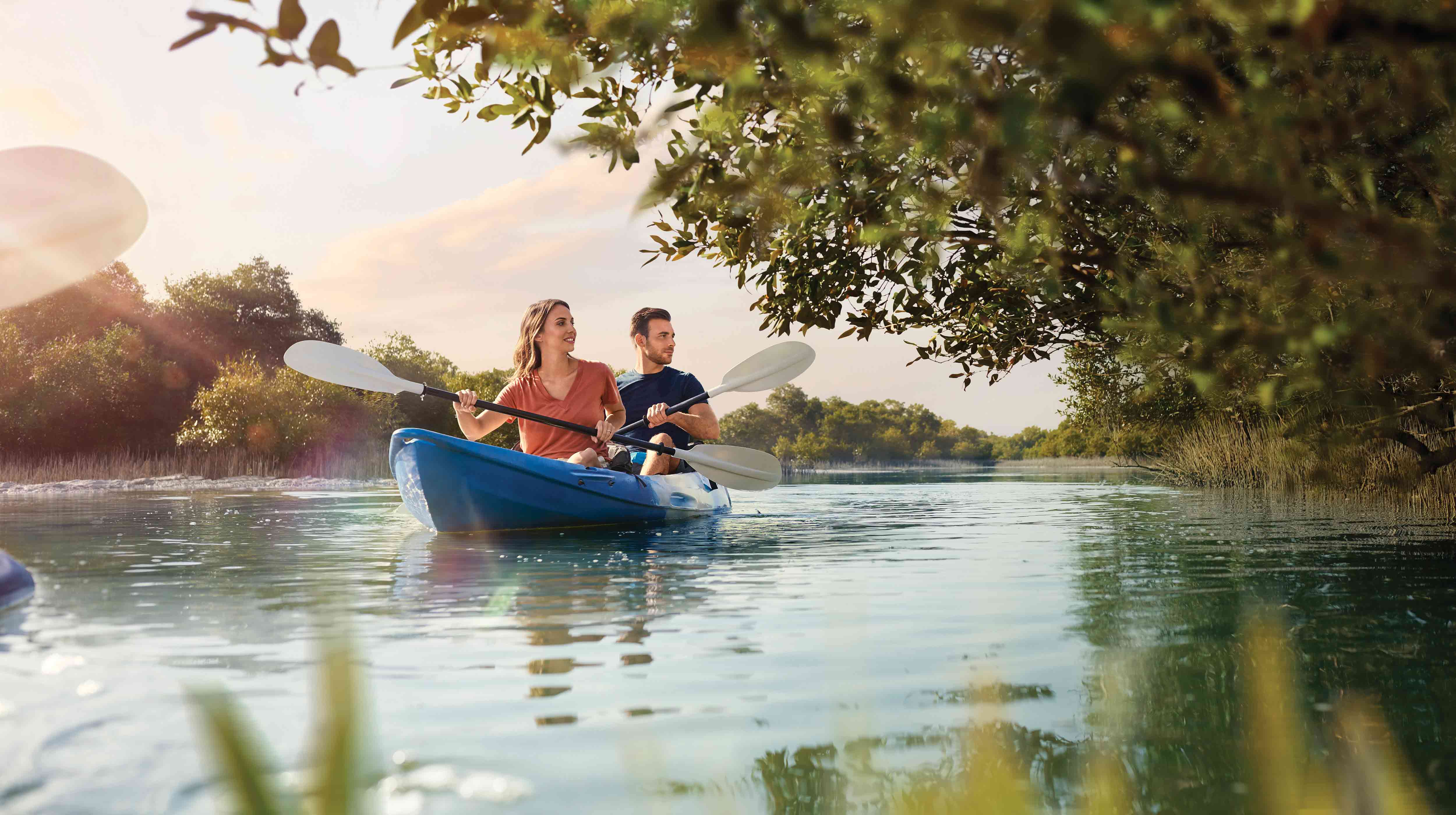 Couple en plein air souriant dans les mangroves d'Abu Dhabi alors qu'ils font du canoë ensemble.