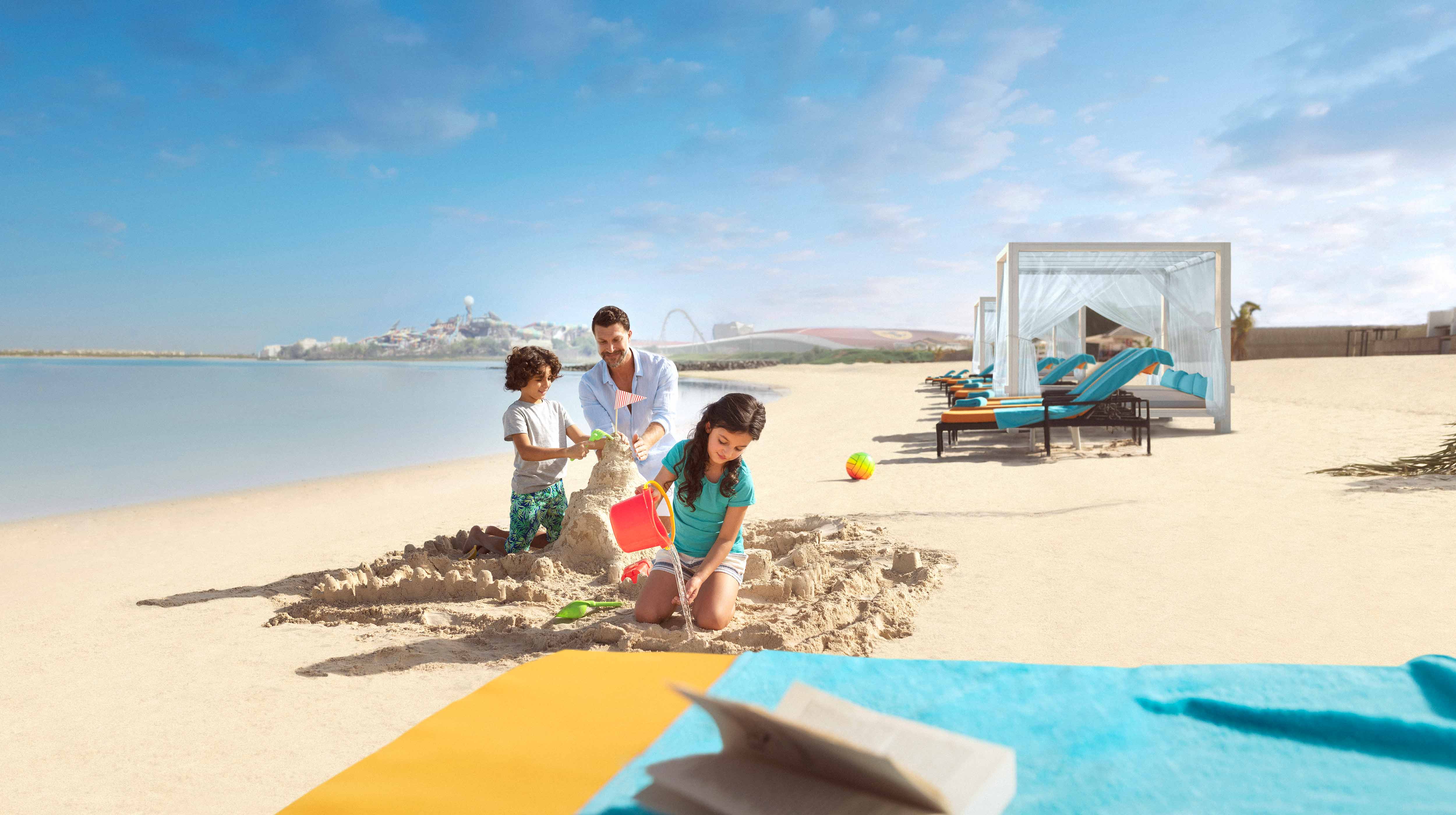 Un uomo, la sua figlia e il suo figlio costruiscono castelli di sabbia nella spiaggia di Abu Dhabi.