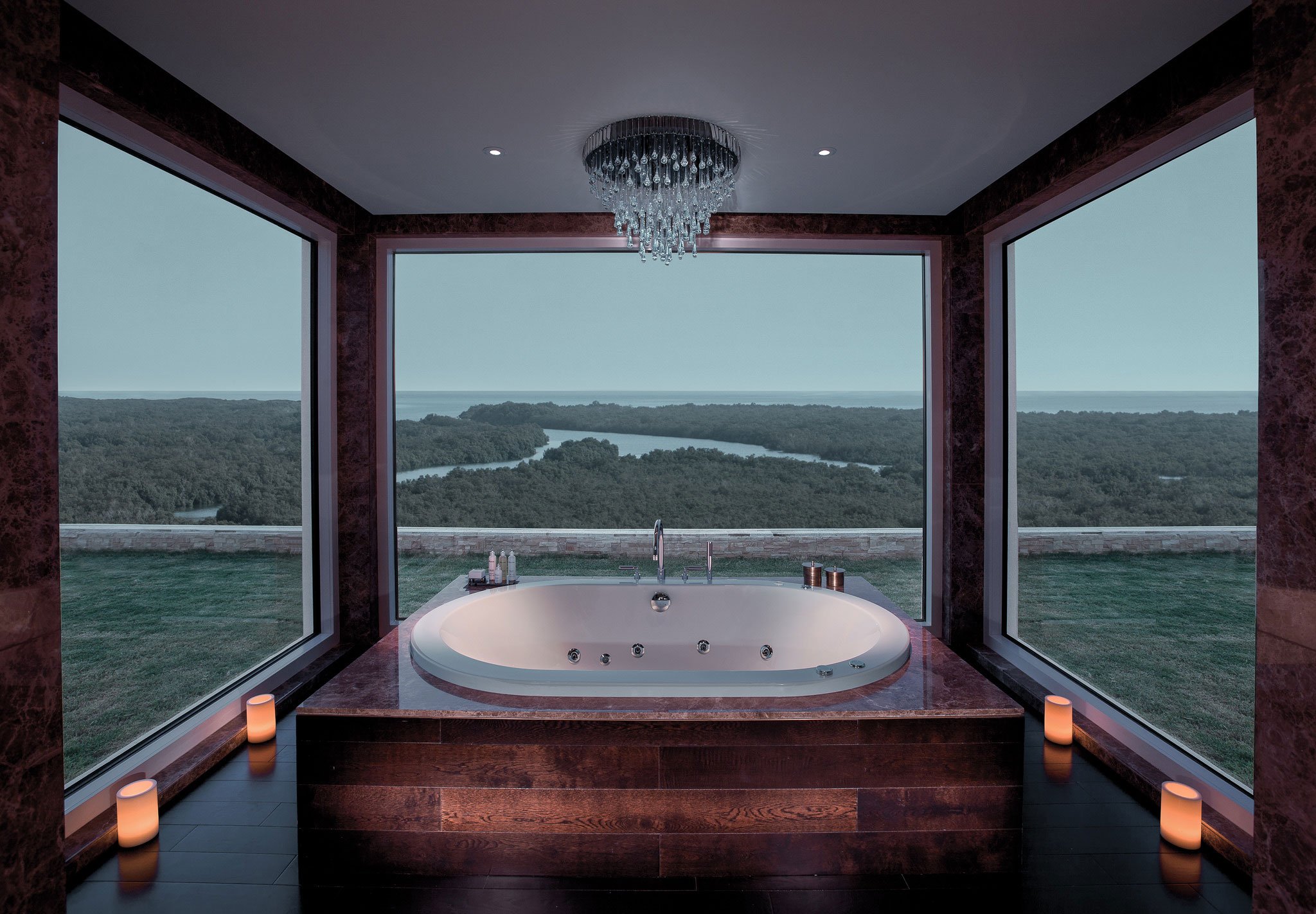 Luxury bathtub with panoramic forest and water views, surrounded by candles and glass