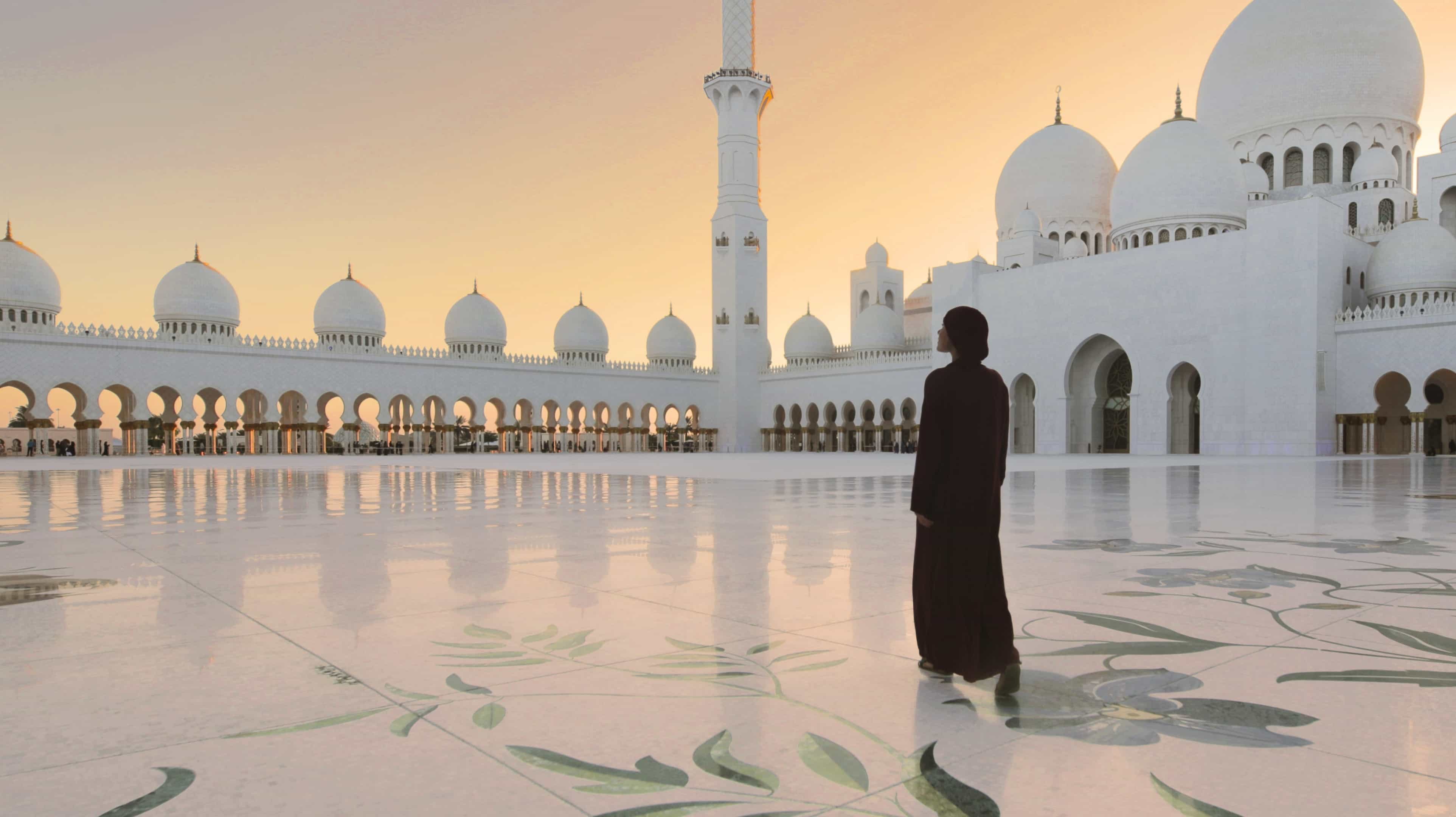 Woman in a black abaya walking in the inner courtyard of the Sheikh Zayed Grand Mosque