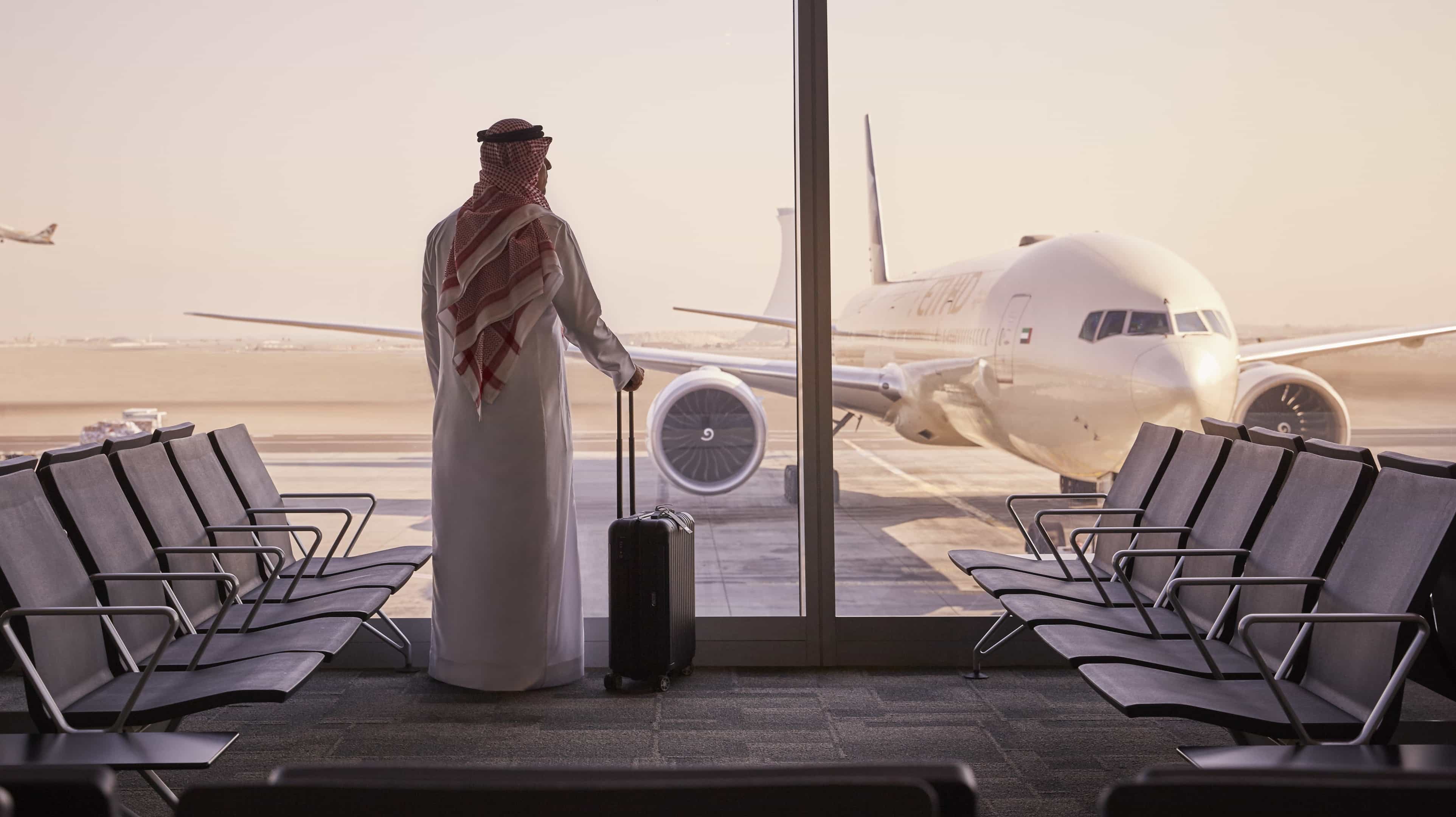 Un uomo in abiti arabi aspetta in un aeroporto. Guarda attraverso il finestrino un aeroplano.