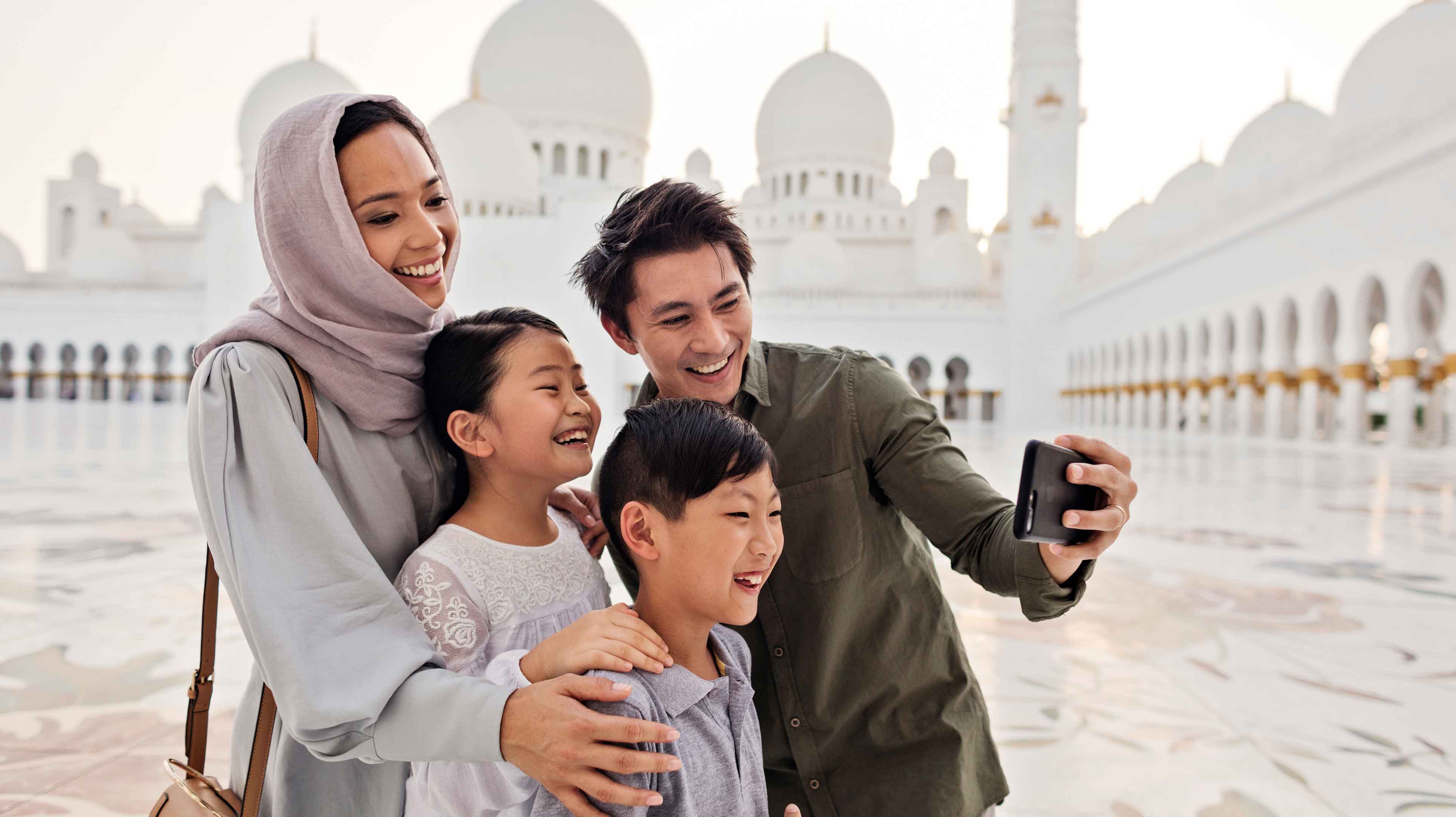 Asian family smiling and taking pictures in Sheikh Zayed Grand Mosque's inner courtyard