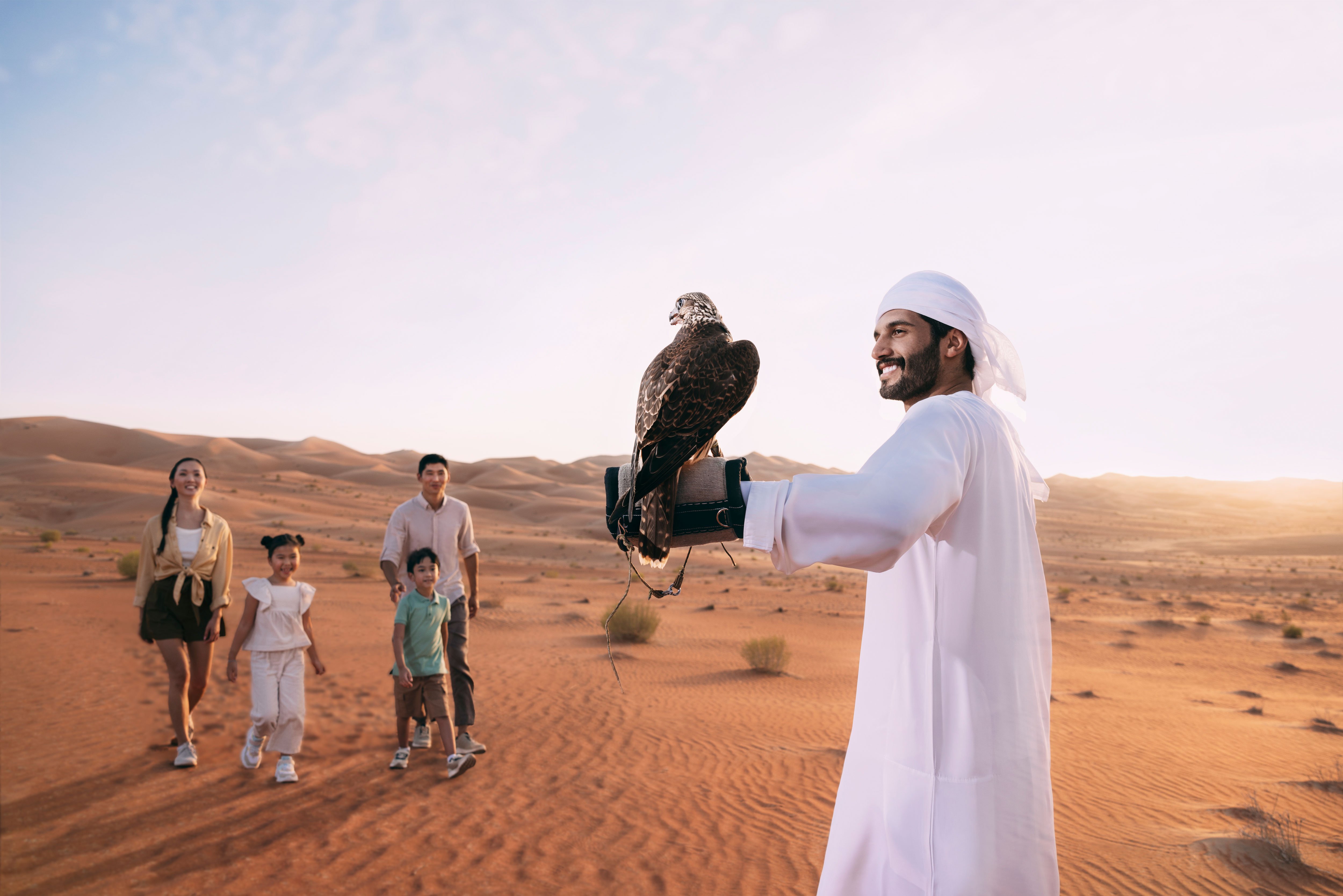 Local guide showing a group of tourists a falcon on his arm in Abu Dhabi desert
