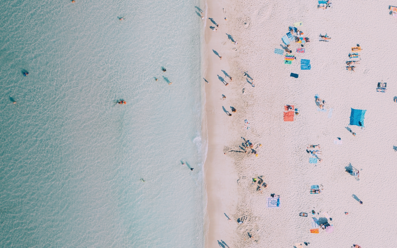 Bird's eye view of a beach where sand and water meet with people on both sides