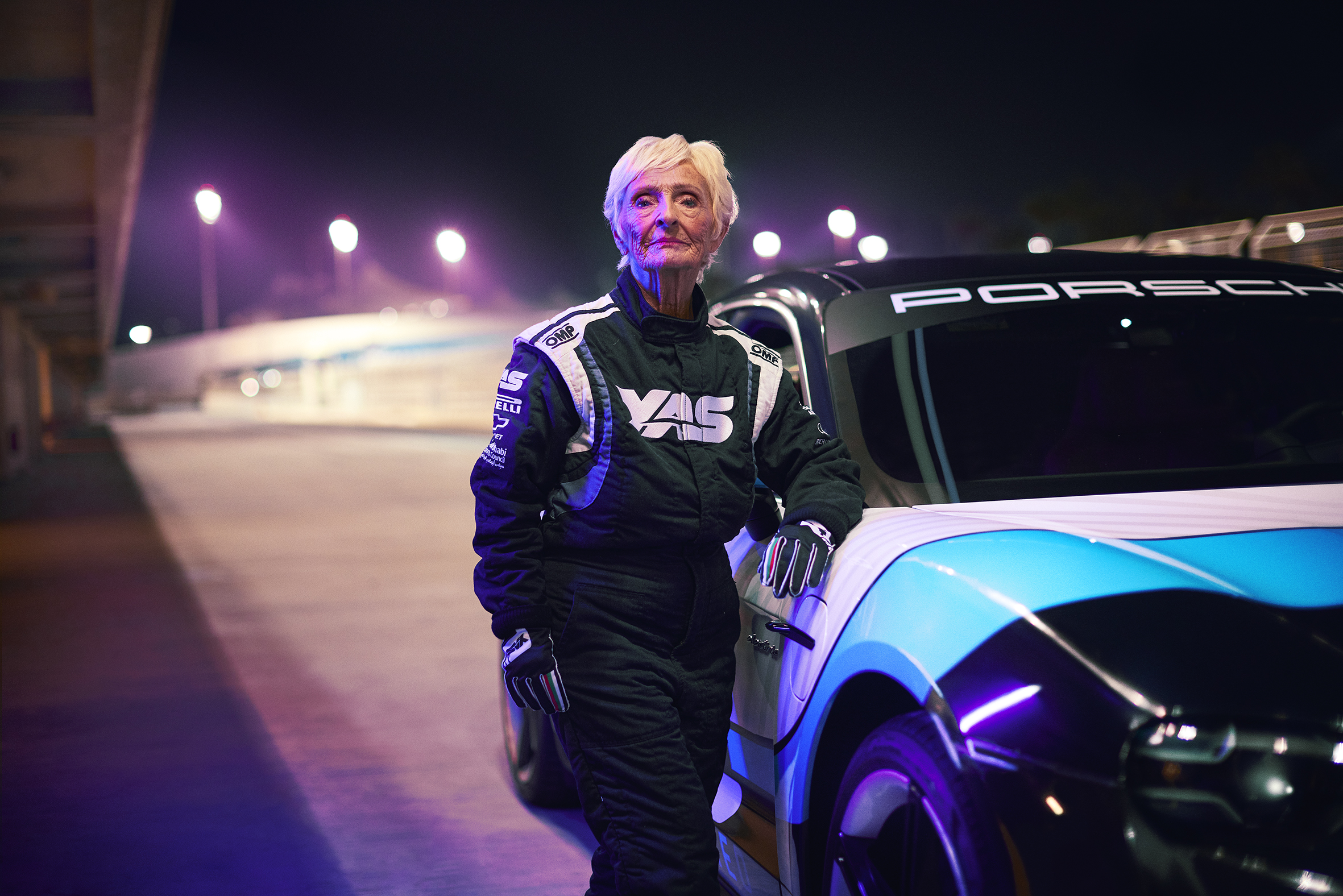 Elderly Western woman in a racing suit standing by a racecar in Yas Marina Circuit