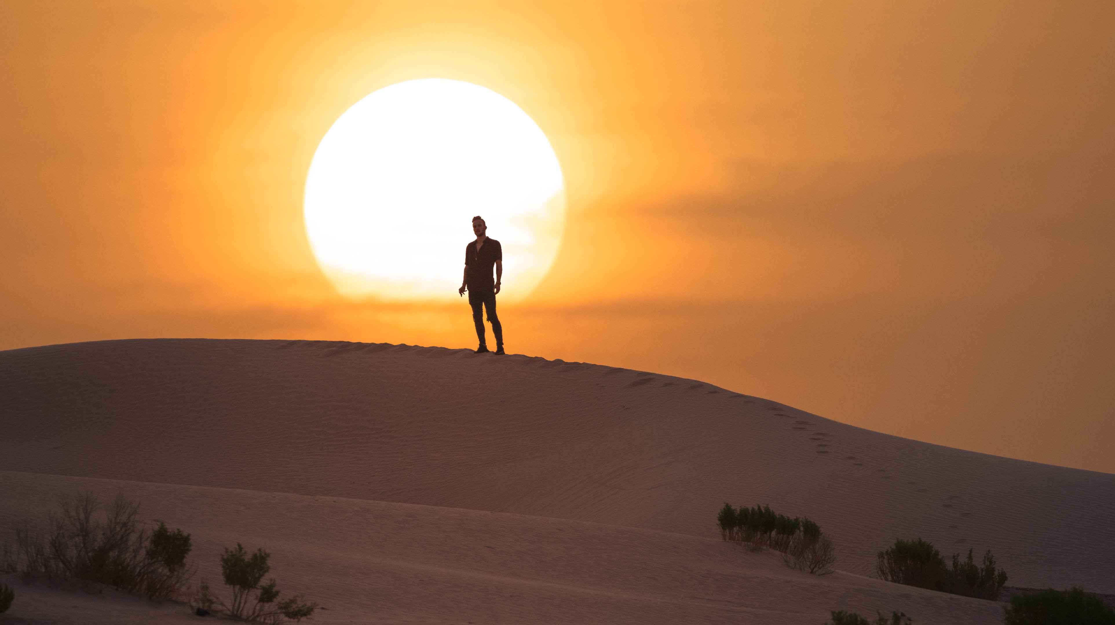 Man standing on a sand dune in the Abu Dhabi desert with the sun rising behind him