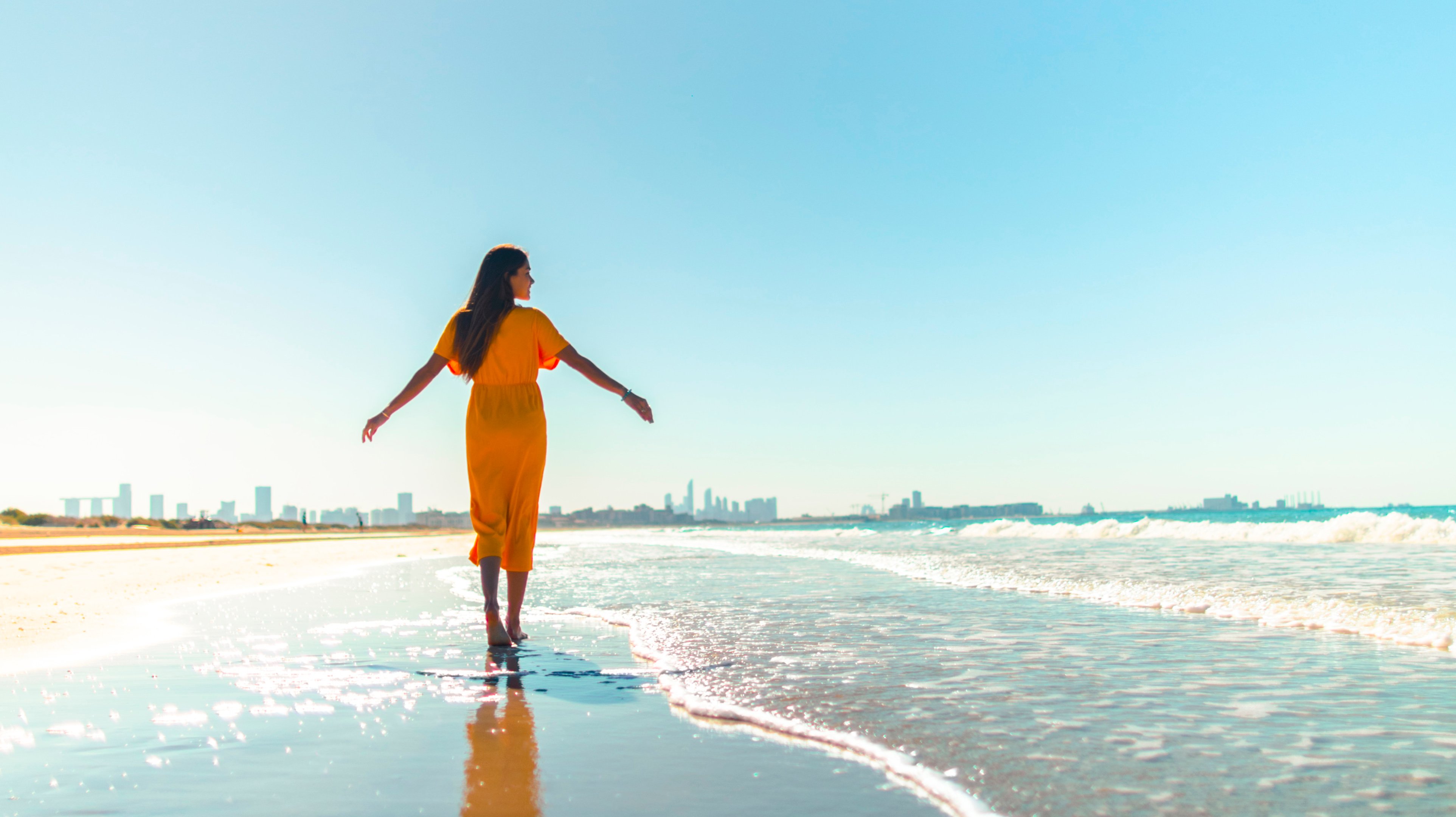 امرأة ترتدي فستان برتقالي وتتمشى على شاطئ البحر