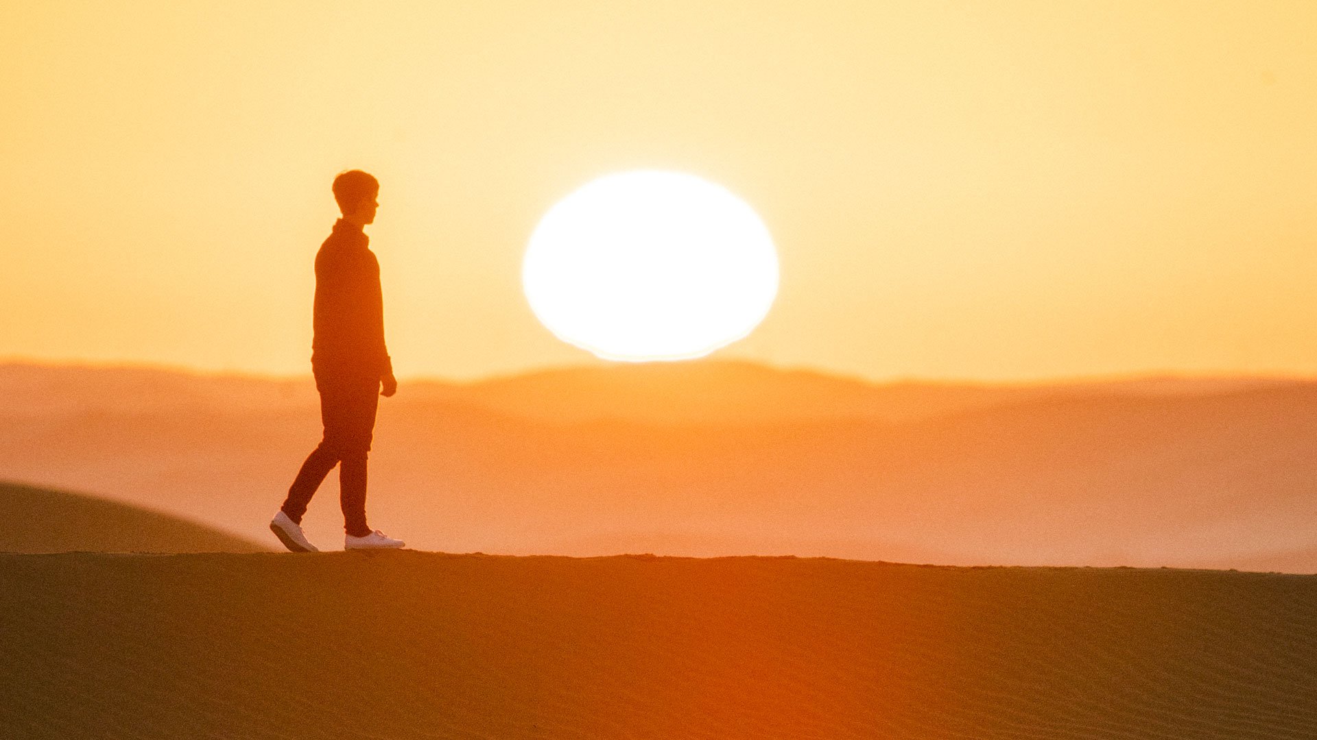 رجل يمشي وسط صحراء أبوظبي أثناء غروب الشمس