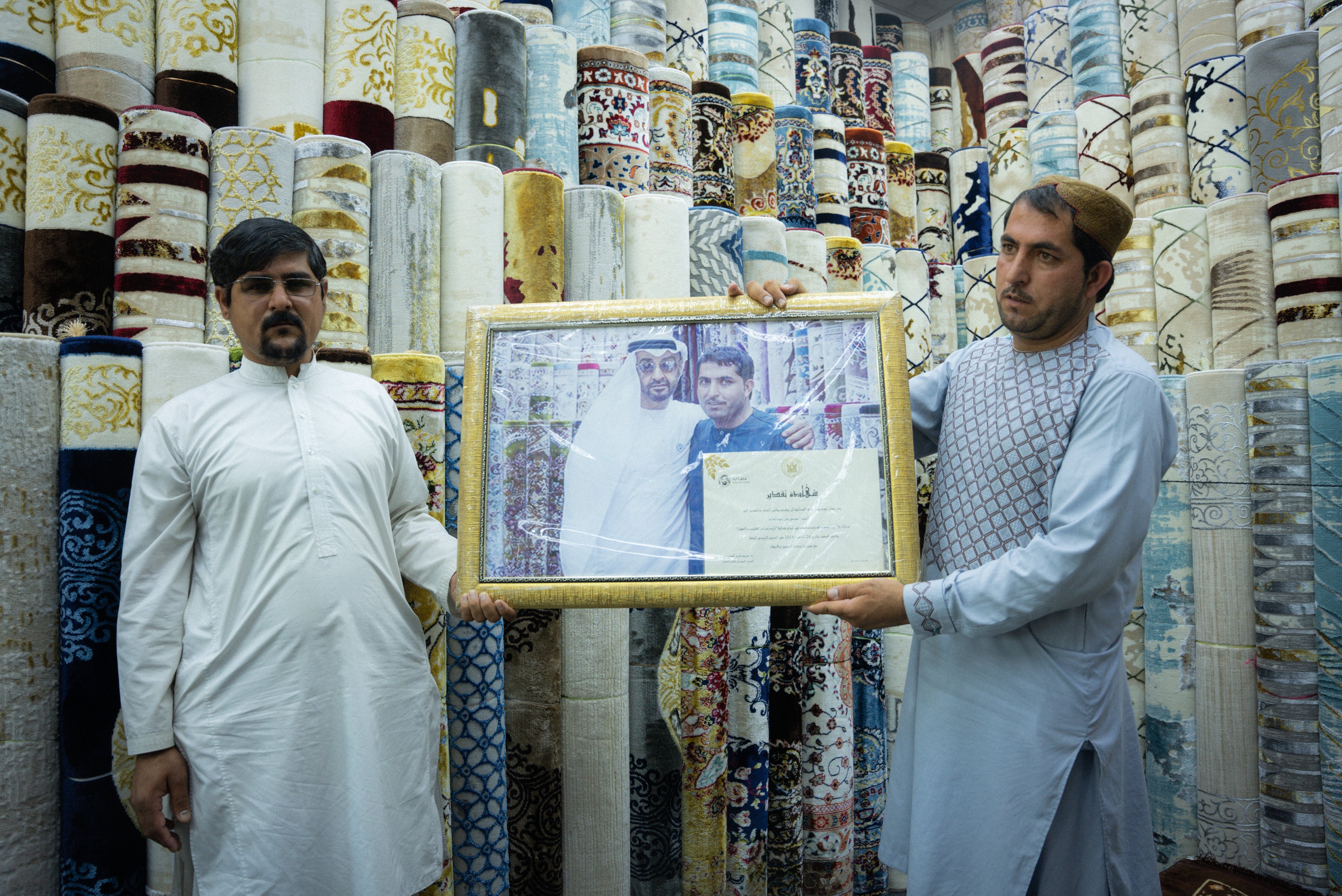 The owner and shopkeeper of Al Safa Carpet shop standing and holding a framed certificate