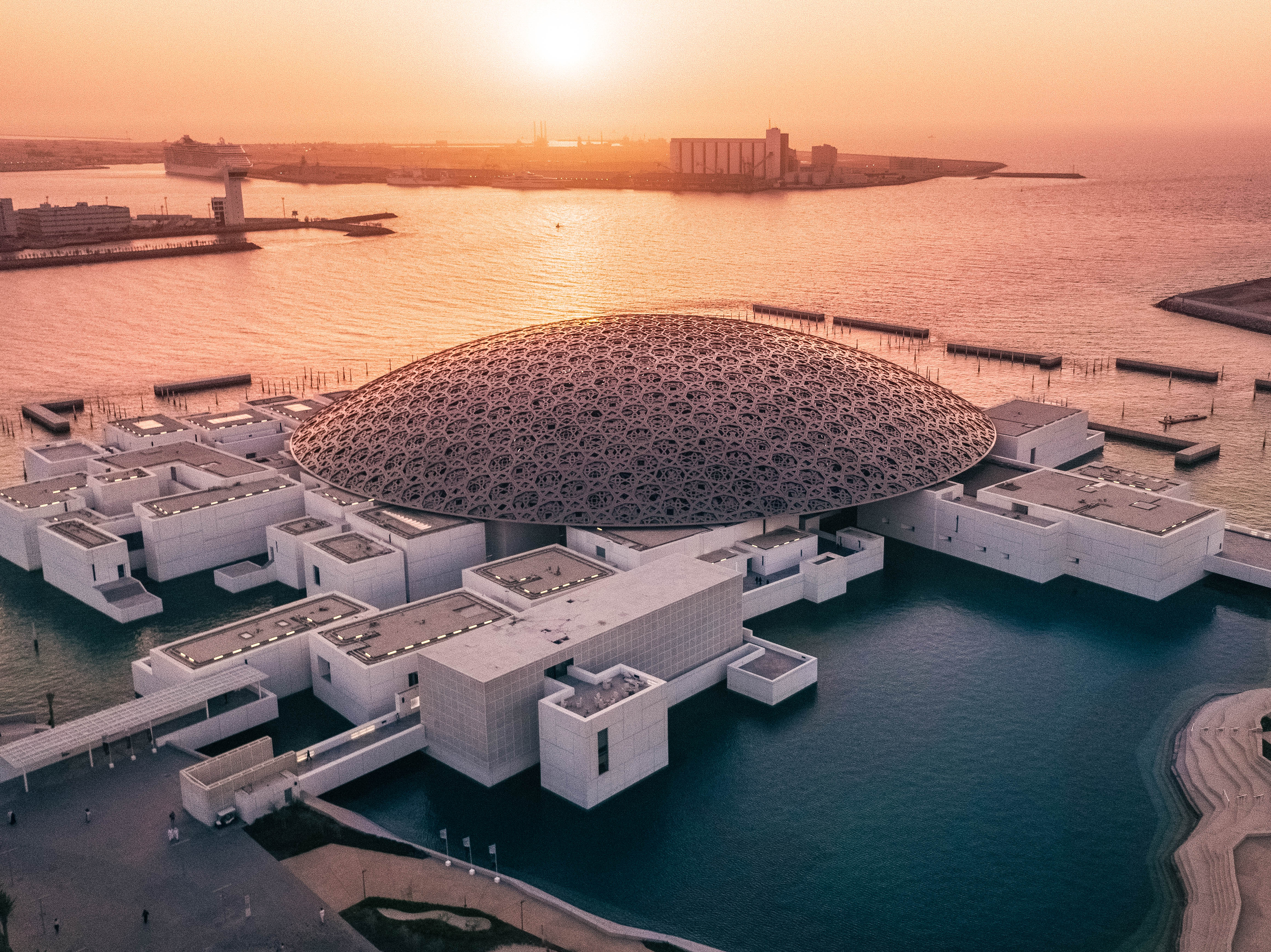 Stunning aerial view of the Louvre Abu Dhabi at sunset, showcasing its iconic dome and waterfront.