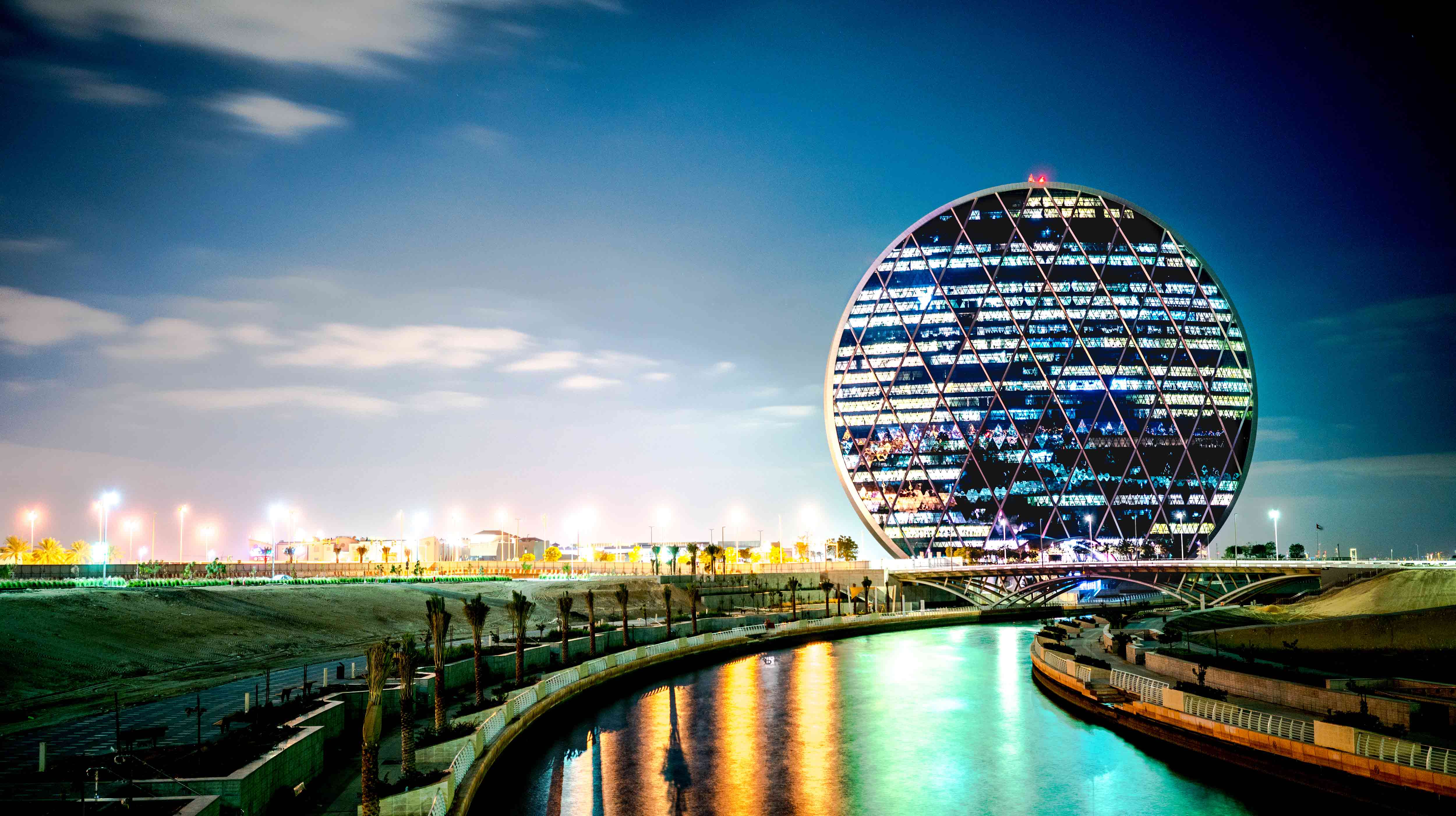 The iconic circular Aldar HQ building in Abu Dhabi in the background behind a stretch of water
