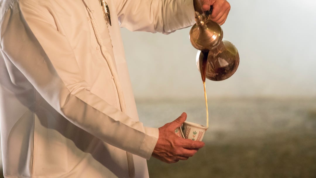 Emirati man's hand pouring traditional Arabic coffee at Qasr Al Hosn
