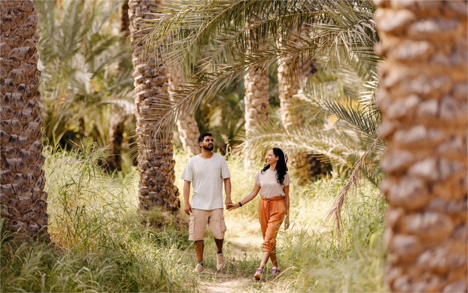 A couple walking between palm trees in the lush green oasis of Al Ain