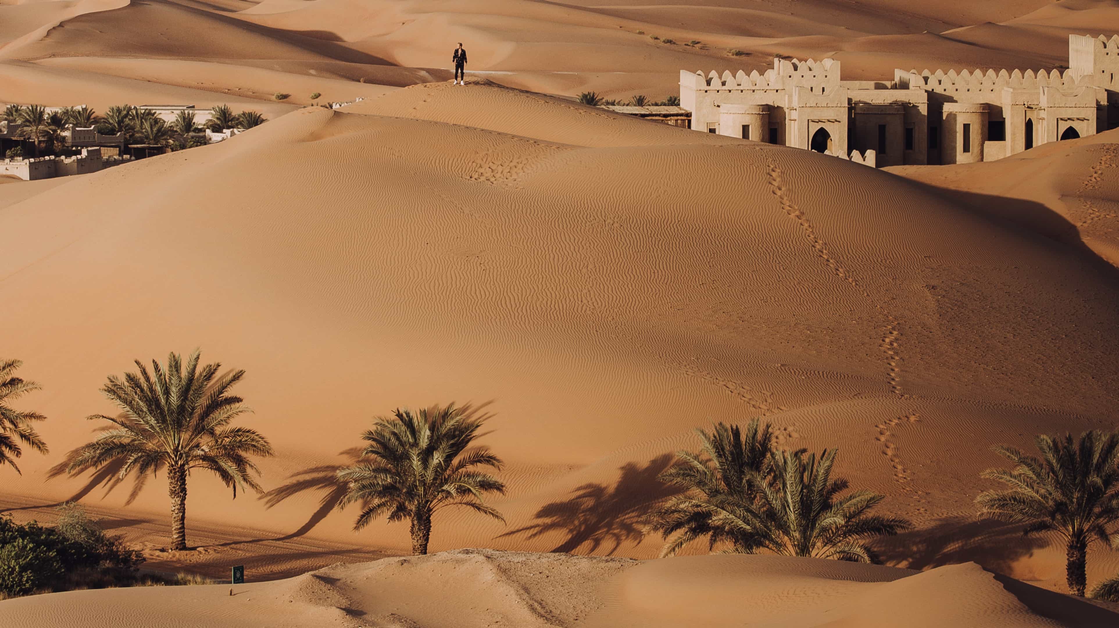 Man standing on the dunes surrounding Qasr Al Sarab Desert Resort by Anantara