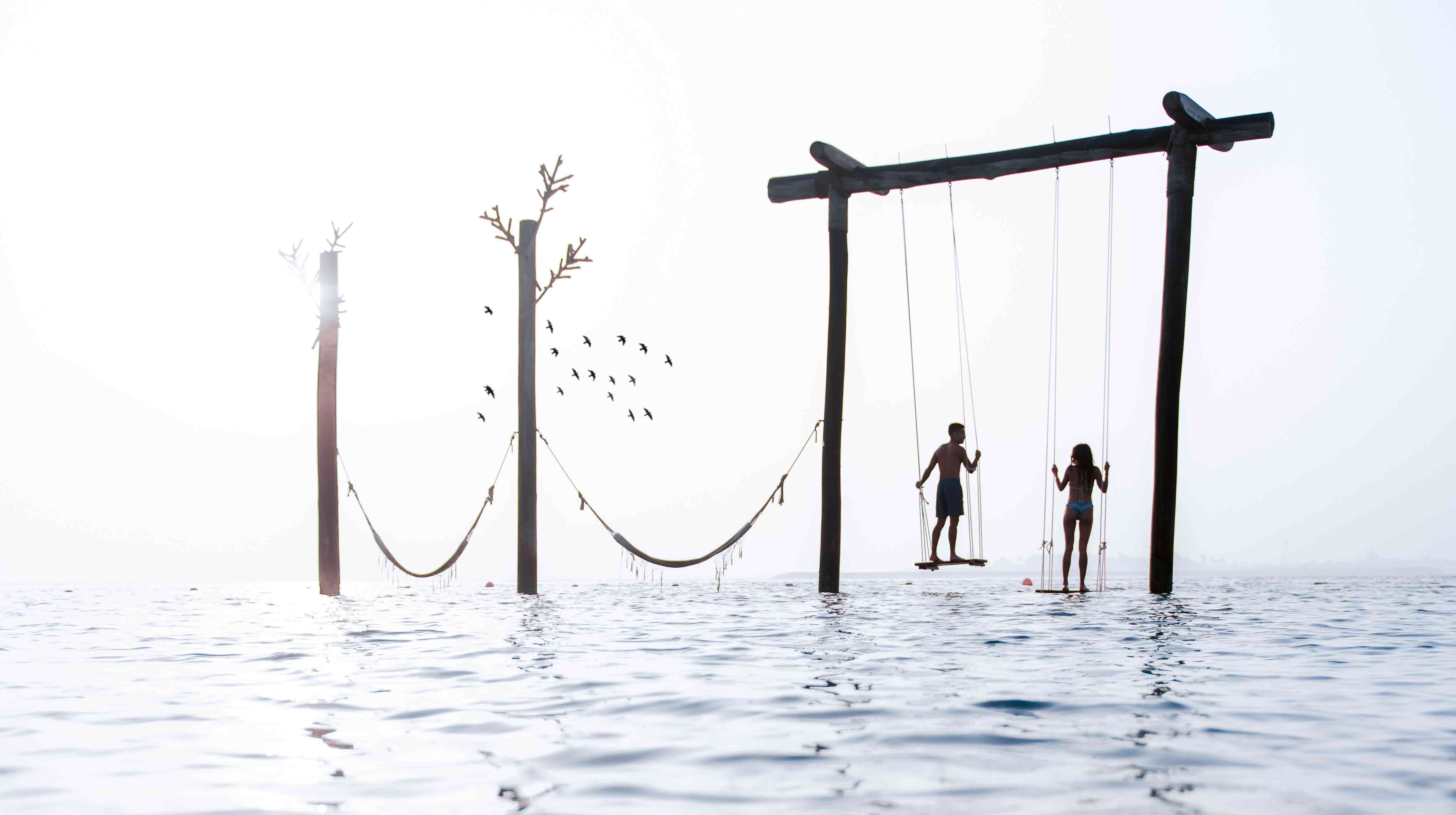 Man and woman standing on swings in the middle of the sea